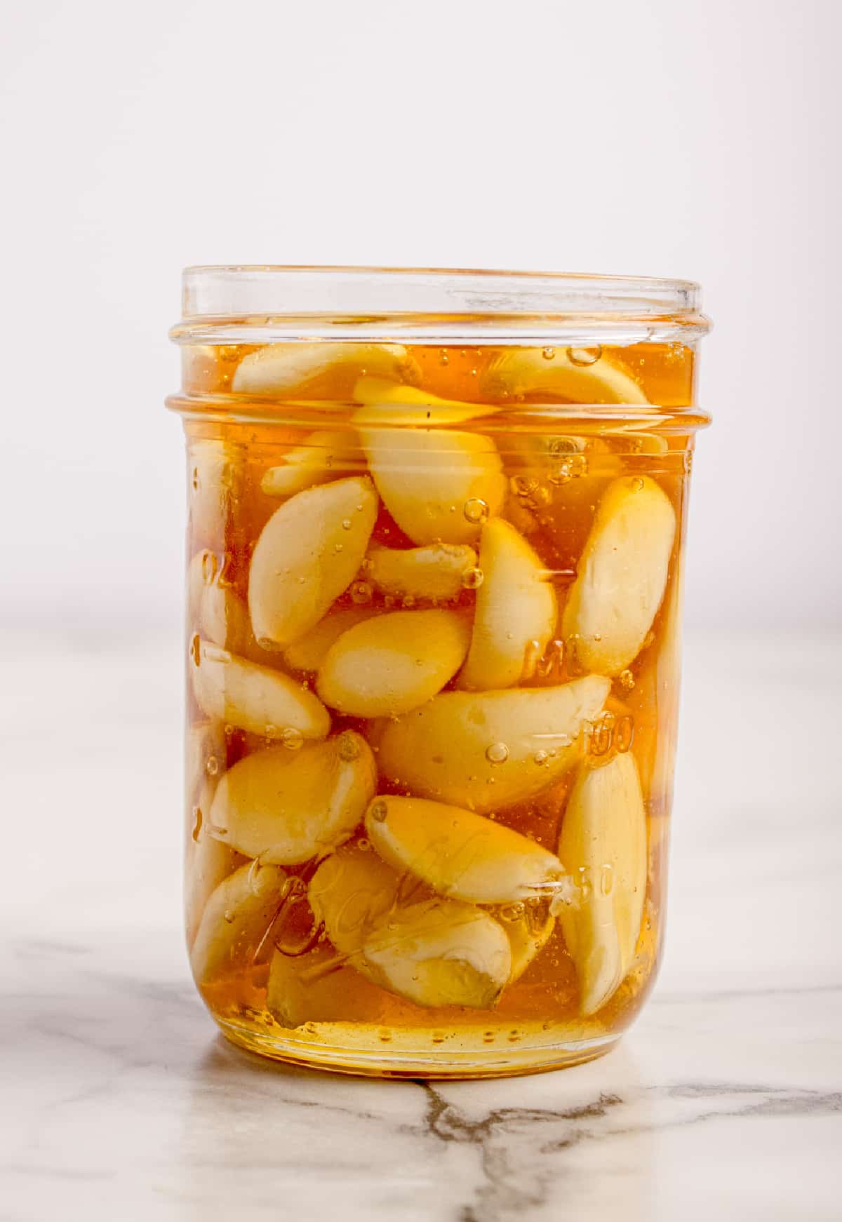 A finished jar of fermented honey garlic showing softened cloves and honey that has thinned during fermentation. Fermented honey garlic after several weeks, with softened whole garlic cloves fully submerged in loosened honey.