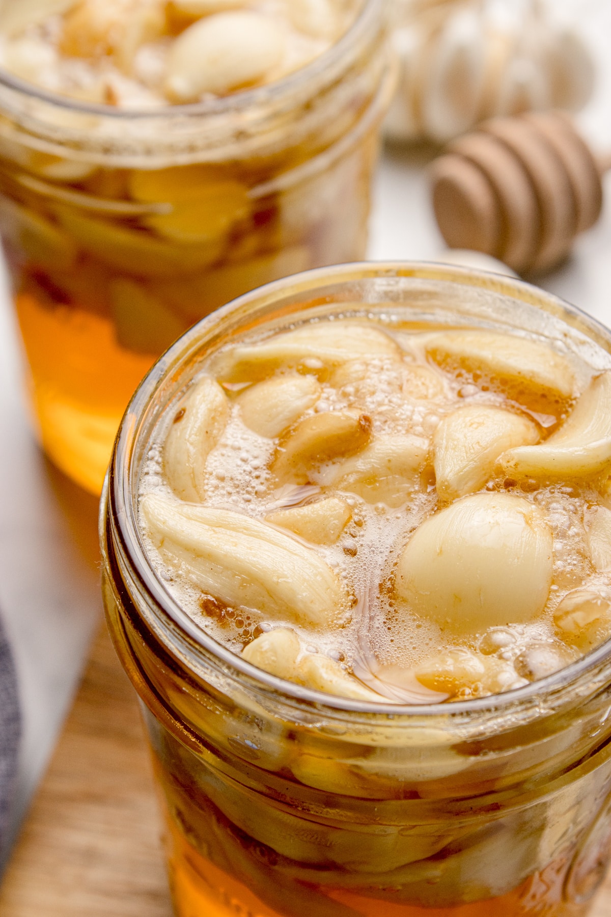 Fermented honey garlic showing active bubbles and softened garlic cloves as the ferment progresses. Fermented honey garlic with whole garlic cloves bubbling in loosened honey near the surface of the jar.