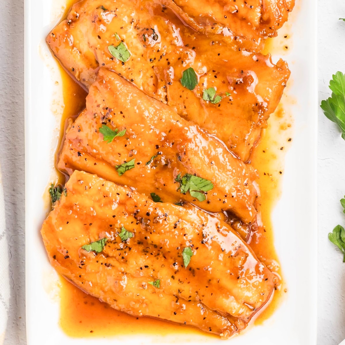 Honey glazed salmon cooked in a smooth honey glaze with butter, soy sauce, and lemon, served on a white platter with parsley.