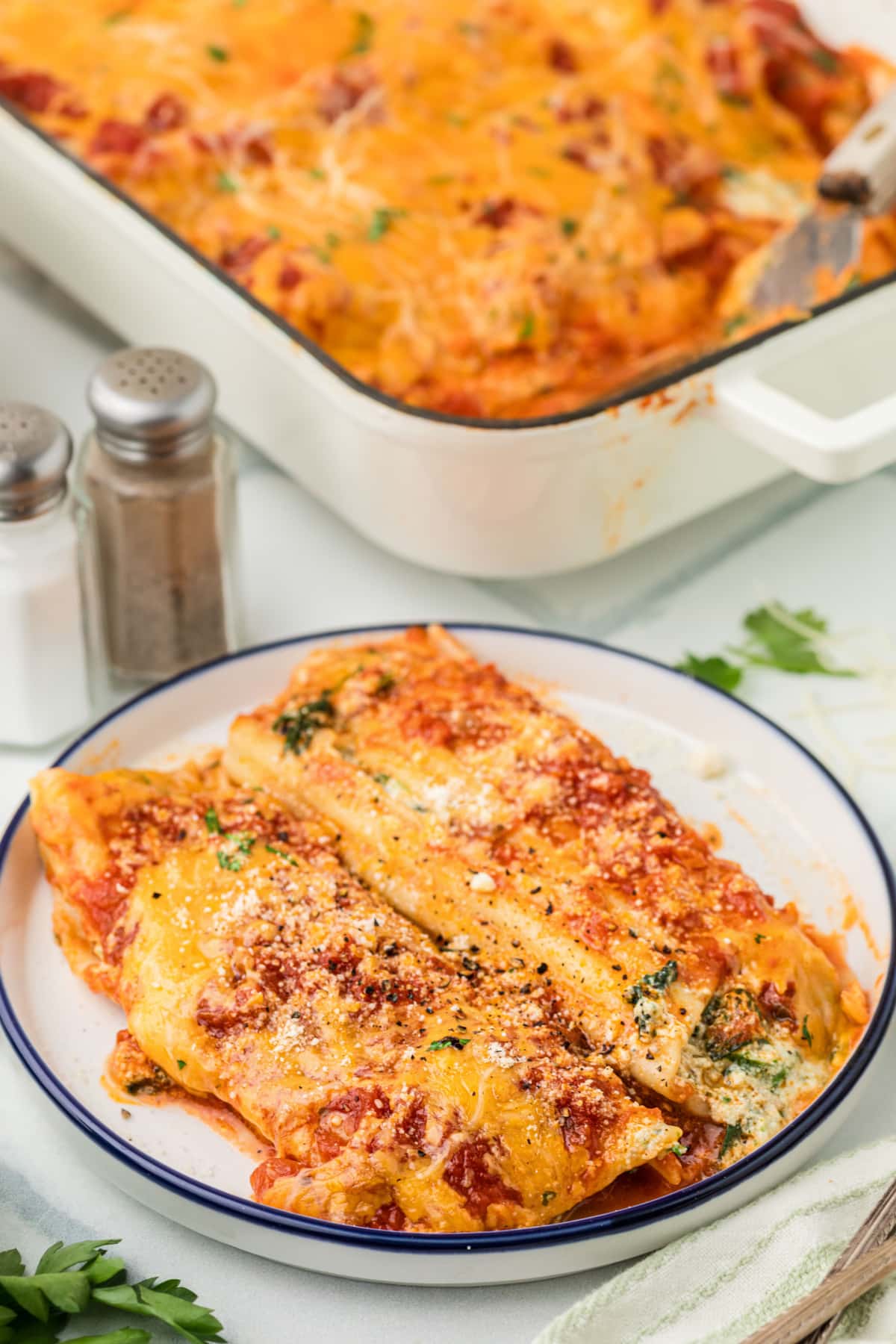 Plated manicotti filled with ricotta and spinach, topped with marinara sauce, melted cheddar, and Parmesan