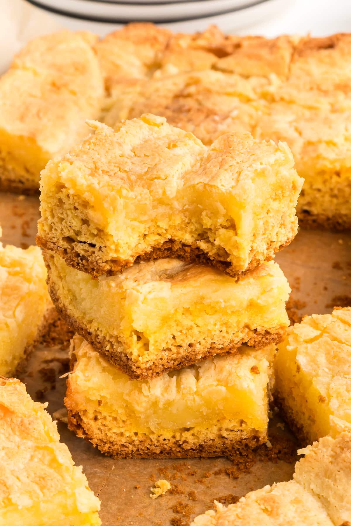 Several cake squares stacked together to show the contrast between the dense base and the creamy top layer. Stacked squares of a cream cheese–topped cake showing the layered base and soft, custardy center, with crumbs scattered on parchment paper.