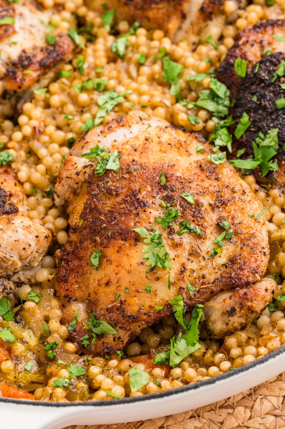 Crispy chicken thighs over pearl couscous baked in a wide pan with lemon, herbs, and vegetables.
