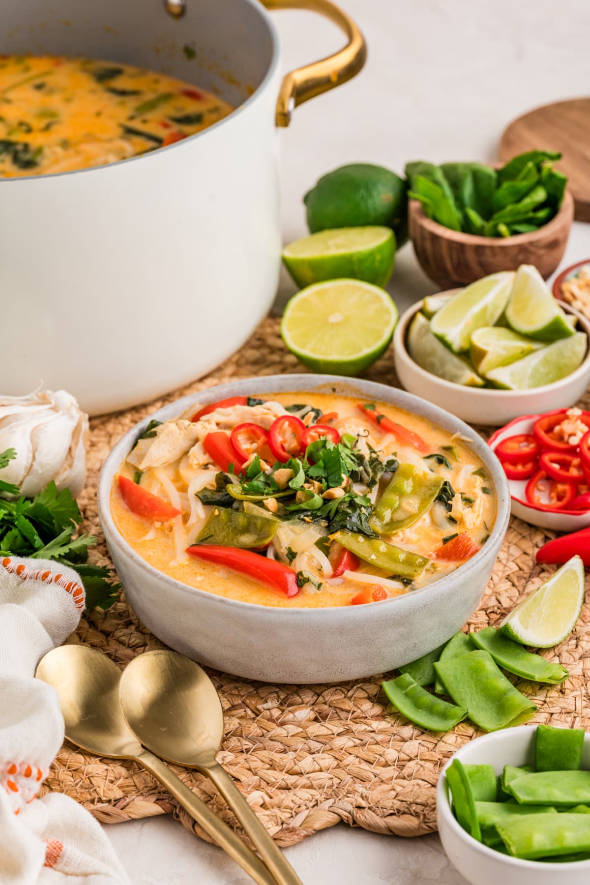 One-pot chicken curry soup with coconut milk, rice noodles, shredded chicken, snow peas, red bell pepper, and fresh herbs, served with lime wedges and chili slices.