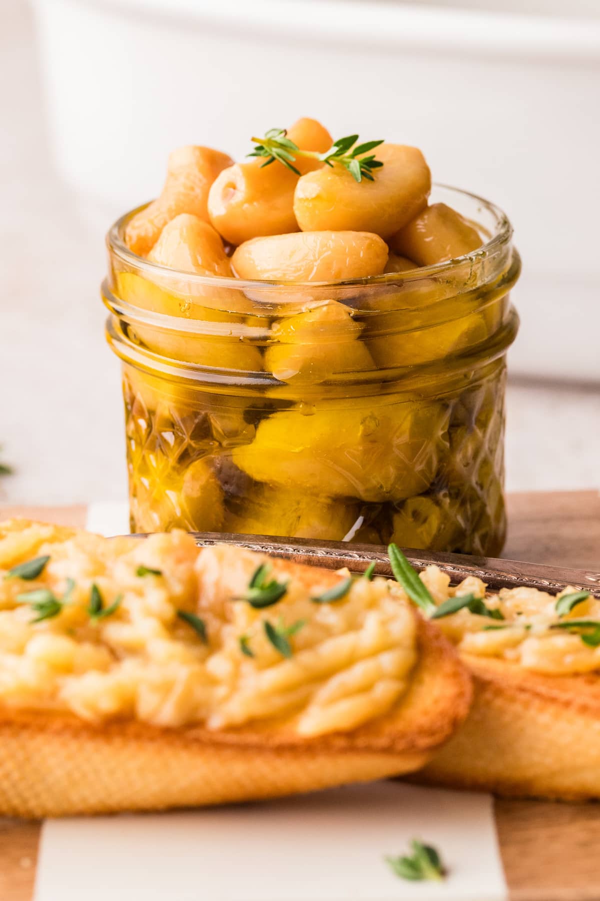 Step-by-step process showing garlic cloves submerged in olive oil before and after slow cooking in the oven.