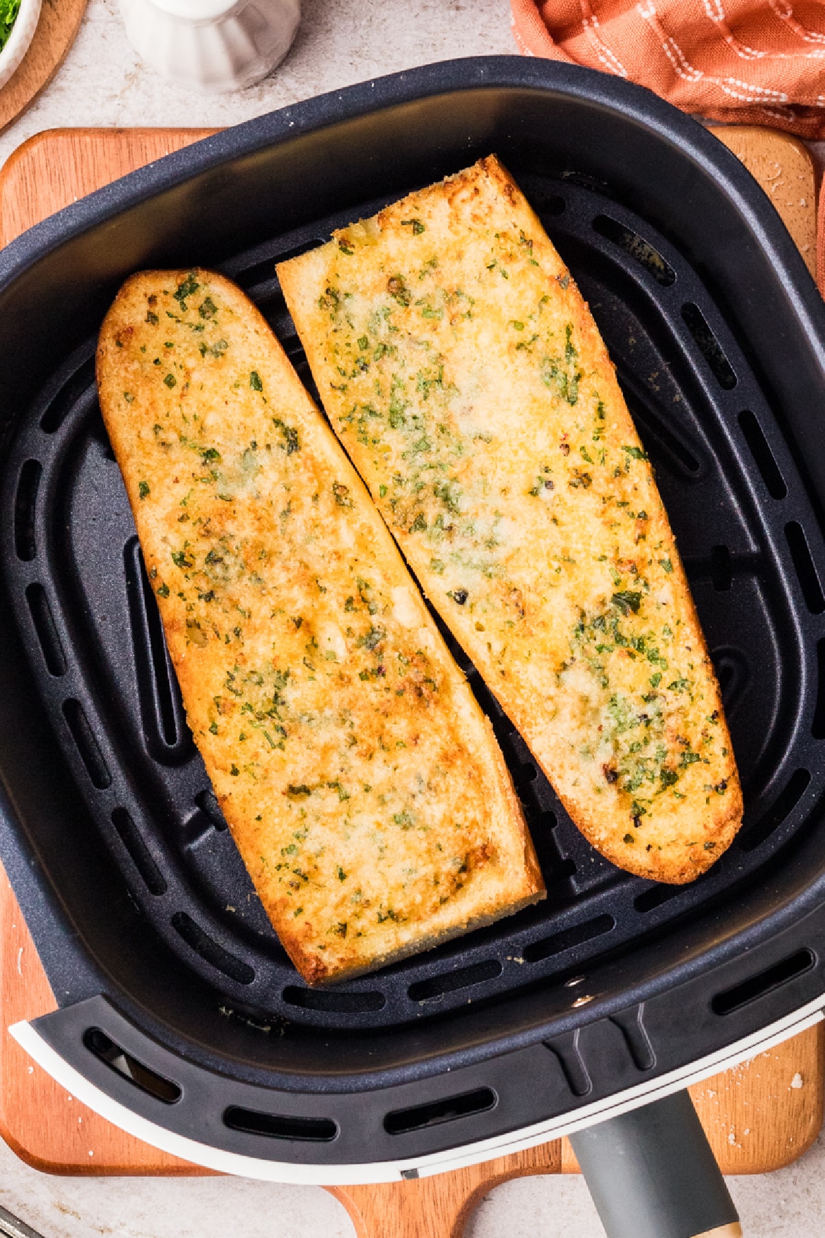 Bread topped with garlic confit butter and Parmesan crisping inside the air fryer basket Garlic confit air fryer bread cooking in the air fryer basket until golden and crisp