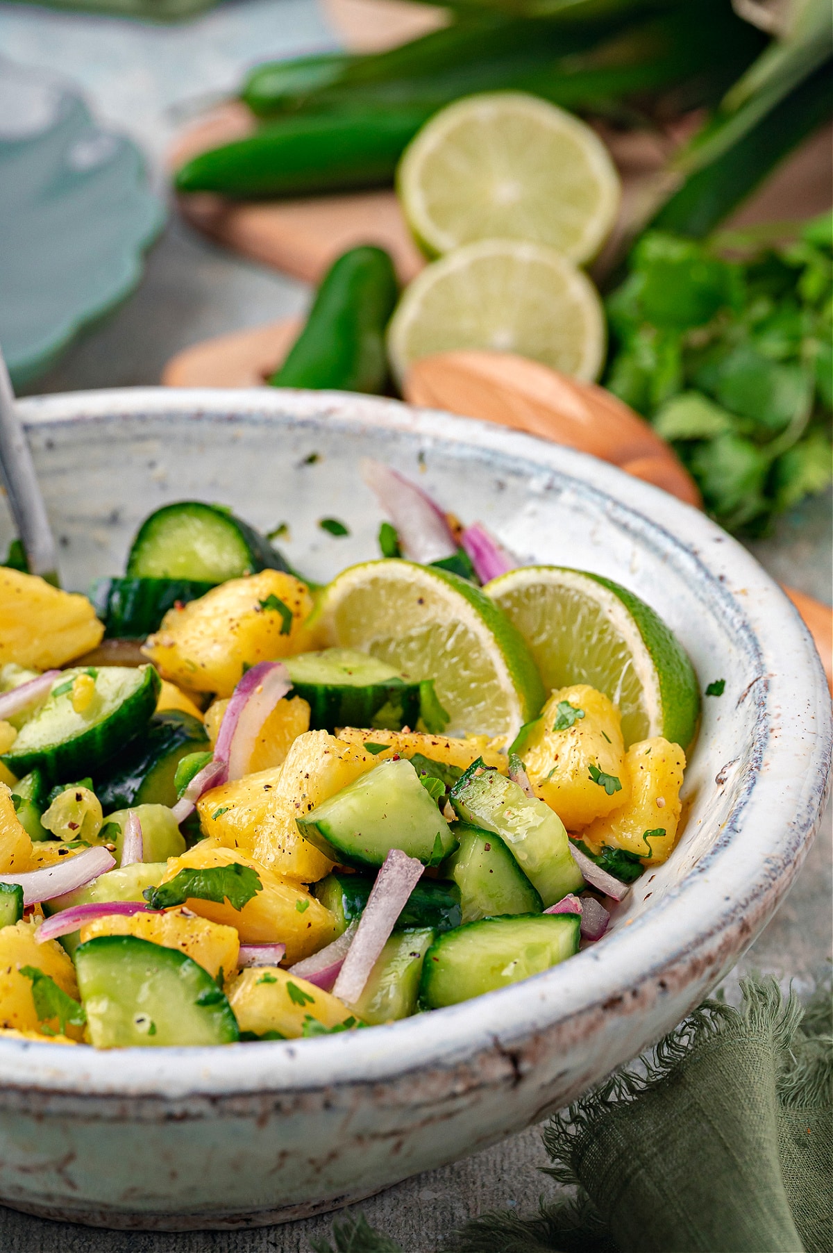Chilled pineapple cucumber salad with fresh pineapple chunks, sliced cucumber, red onion, cilantro, and lime slices in a ceramic bowl.
