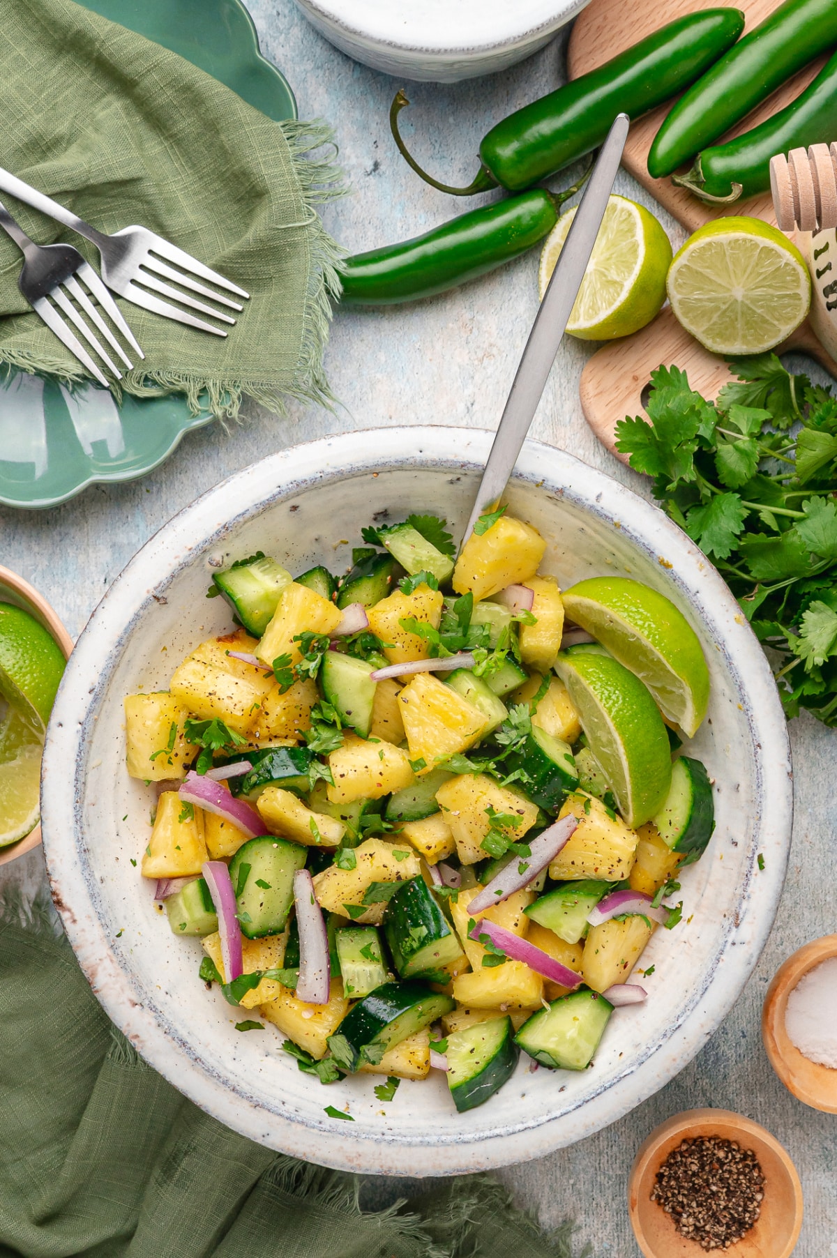 Chilled pineapple cucumber salad with fresh pineapple, cucumber, red onion, serrano pepper, cilantro, and lime wedges in a bowl.