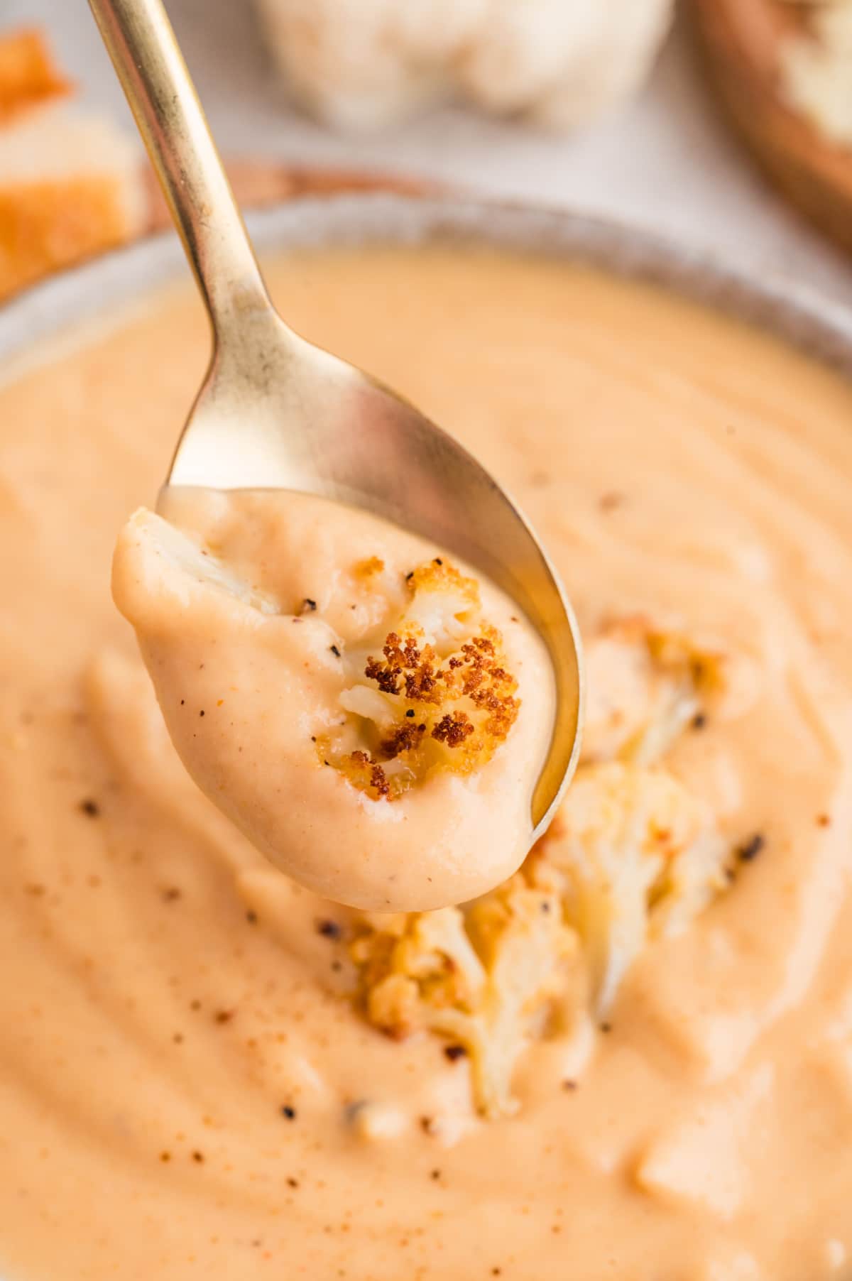 A close-up spoonful of creamy cauliflower soup showing its smooth texture and roasted cauliflower garnish. A spoonful of creamy cauliflower soup with a piece of roasted cauliflower lifted from the bowl.