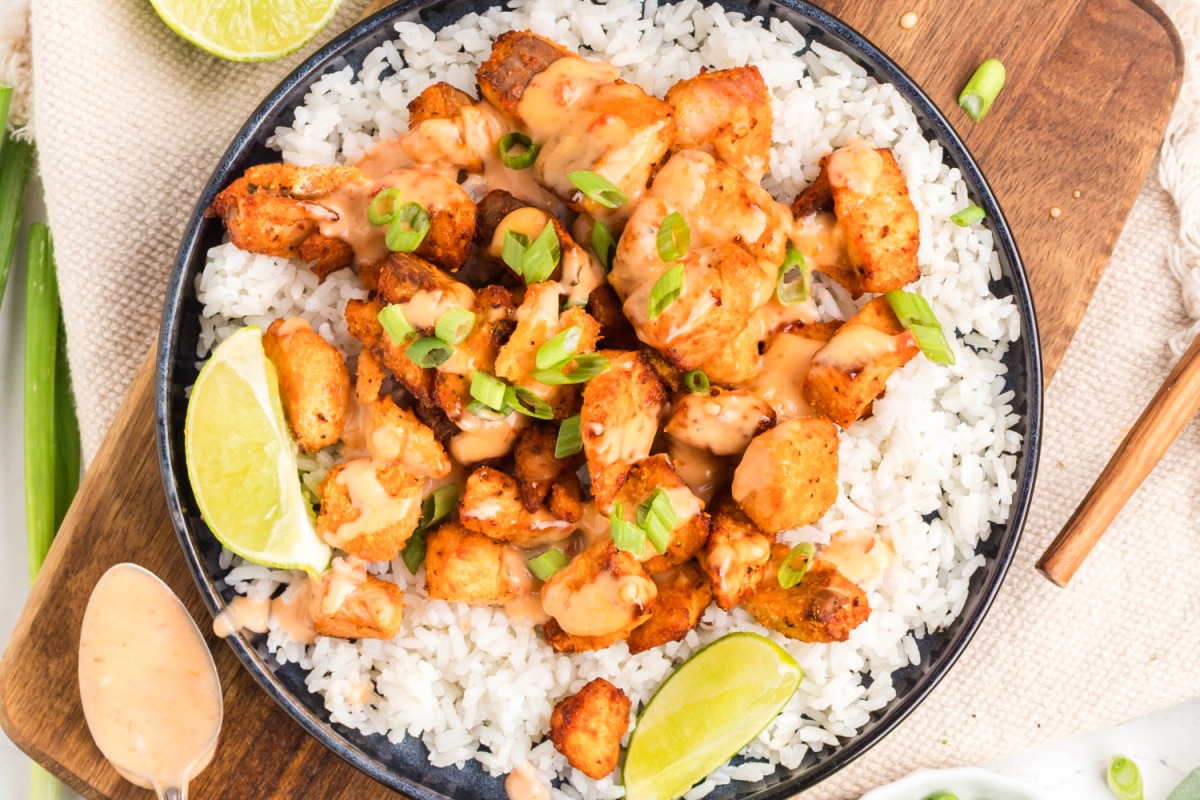 Air fryer bang bang salmon bites served over white rice with creamy sauce, sliced green onions, and lime wedges.