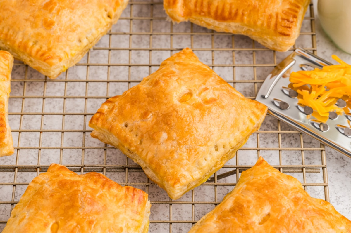 Golden puff pastry breakfast pastries cooling on a wire rack with visible flaky layers and sealed edges.