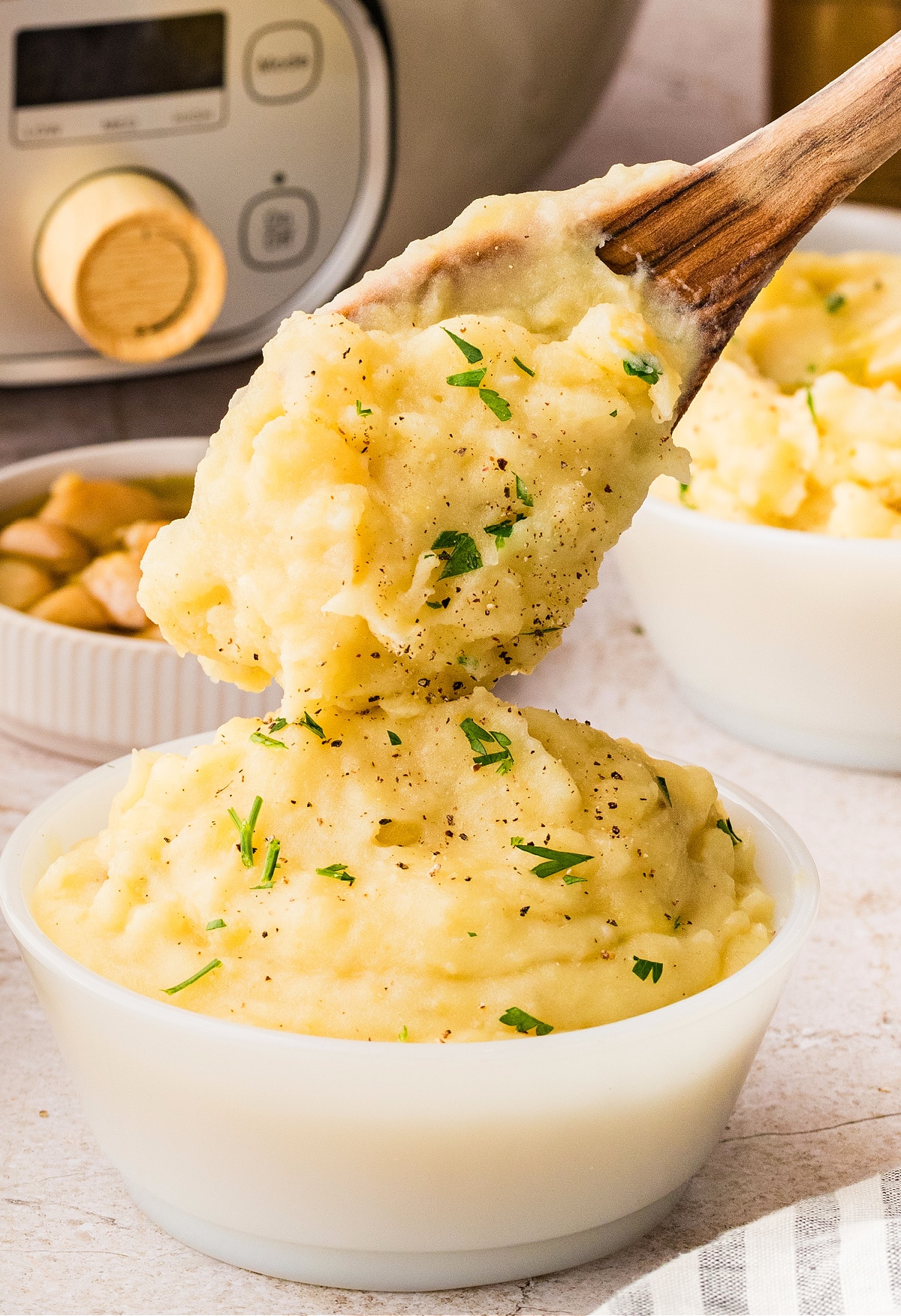 Creamy mashed potatoes being scooped with a wooden spoon, showing a soft texture and light seasoning while held warm.