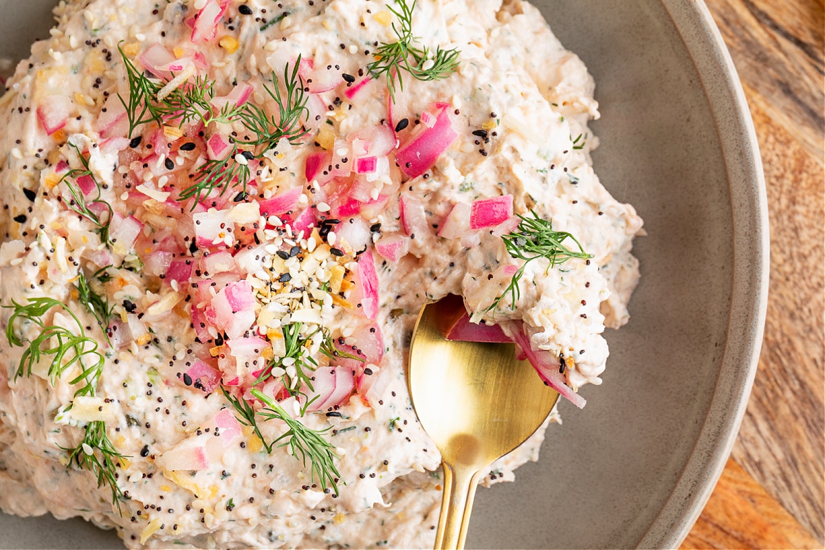 Creamy salmon dip topped with pickled red onions, fresh dill, and everything bagel seasoning, styled on a serving board with lemon halves.
