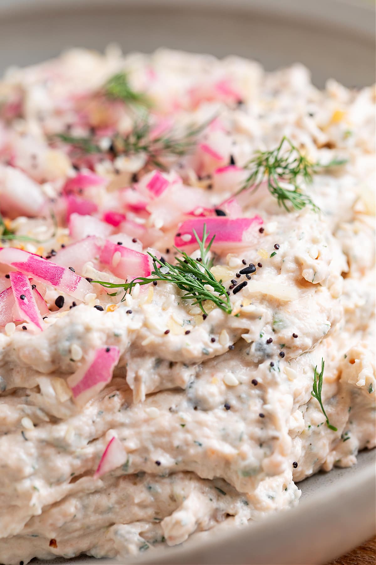 Close-up of smoked salmon dip showing a chunky, creamy texture with pickled red onions, fresh dill, and everything bagel seasoning on top.