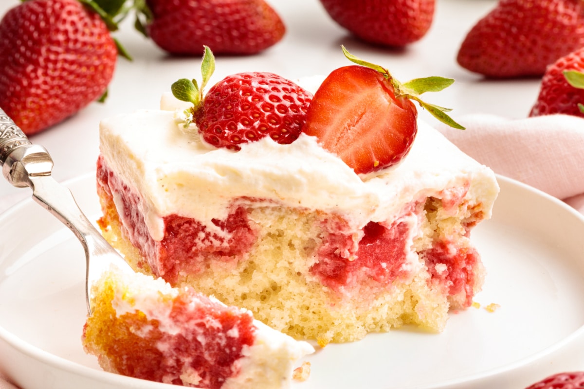 Strawberry Jell-O poke cake bite showing soaked strawberry filling, soft white cake, and whipped vanilla cream cheese frosting on a fork.
