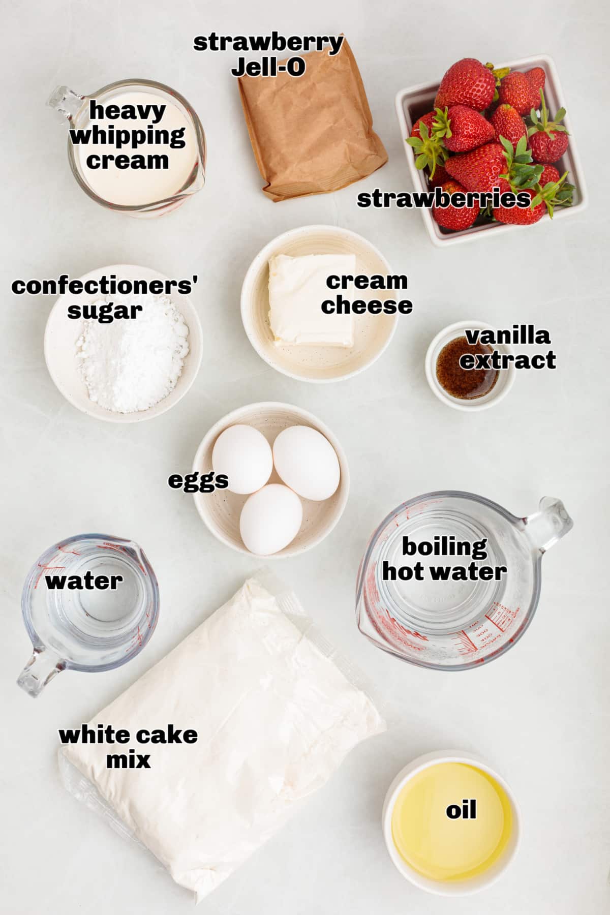Ingredients for strawberry Jell-O poke cake arranged on a light surface, including white cake mix, eggs, oil, water, strawberry gelatin, fresh strawberries, cream cheese, confectioners’ sugar, vanilla extract, and heavy whipping cream.