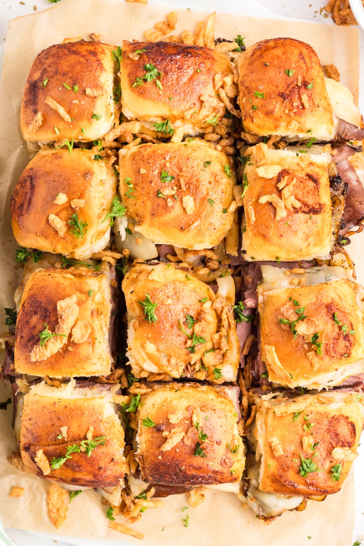 Overhead pull-apart sliders made with roast beef, provolone cheese, caramelized onions, and French-fried onions baked on sweet rolls Pull-apart roast beef sliders baked on sweet rolls with melted provolone and caramelized onions