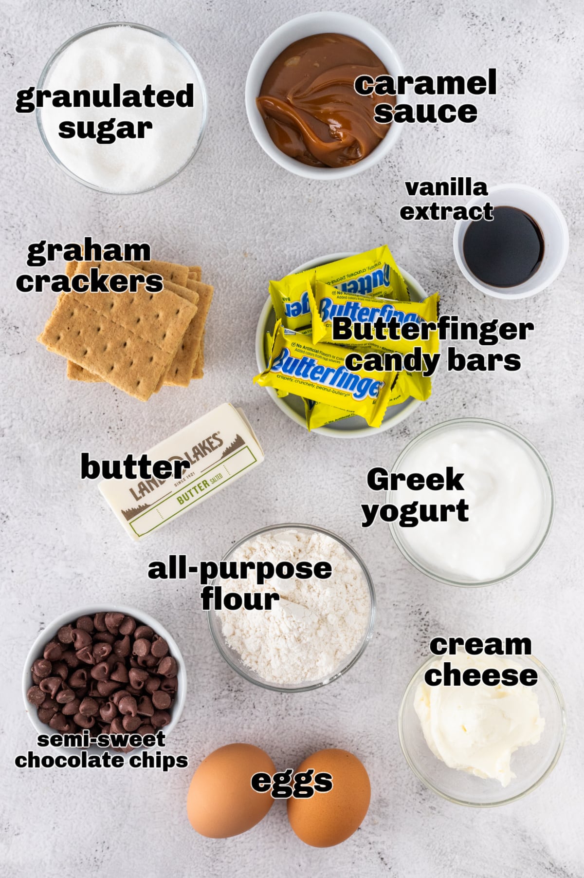 Ingredients for Butterfinger Caramel Cheesecake Bars including graham crackers, cream cheese, caramel sauce, Butterfinger candy bars, and chocolate chips