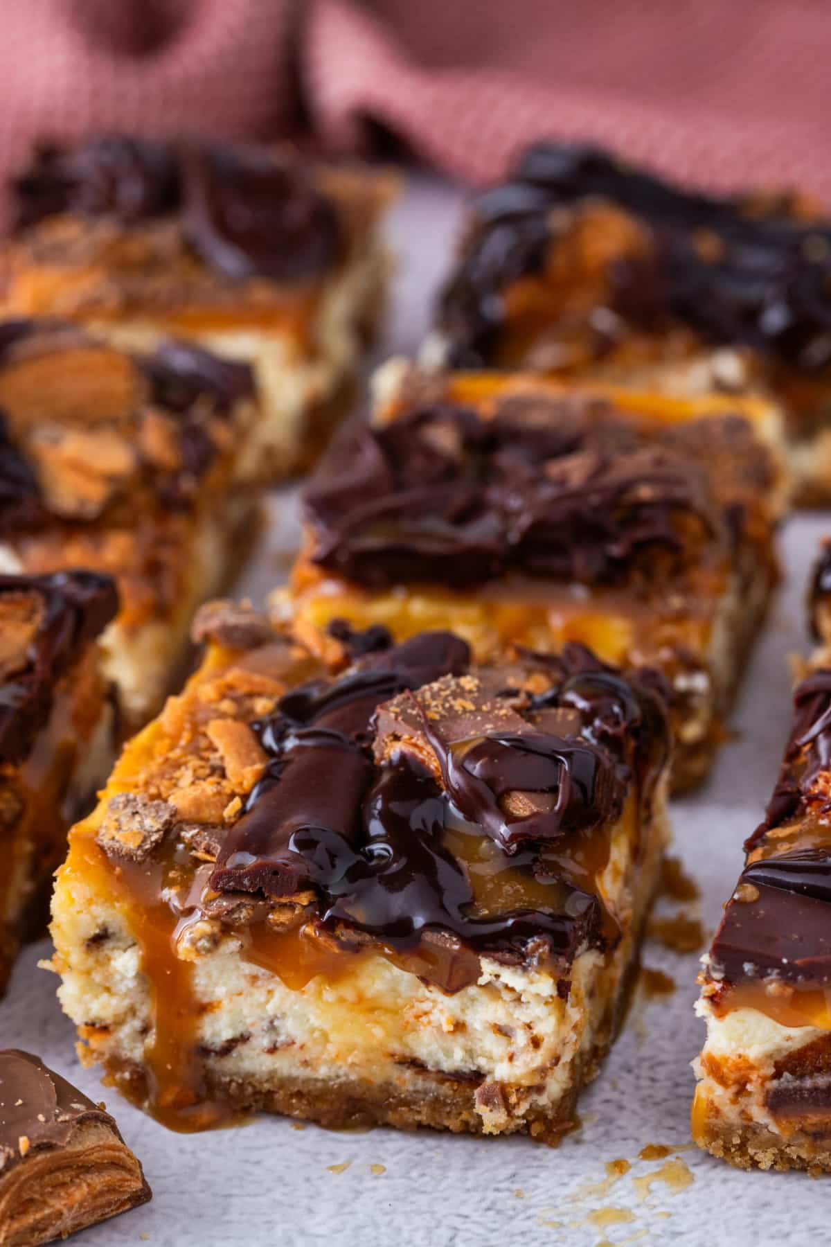 Caramel cheesecake bars with chopped Butterfinger candy and chocolate drizzle on top
