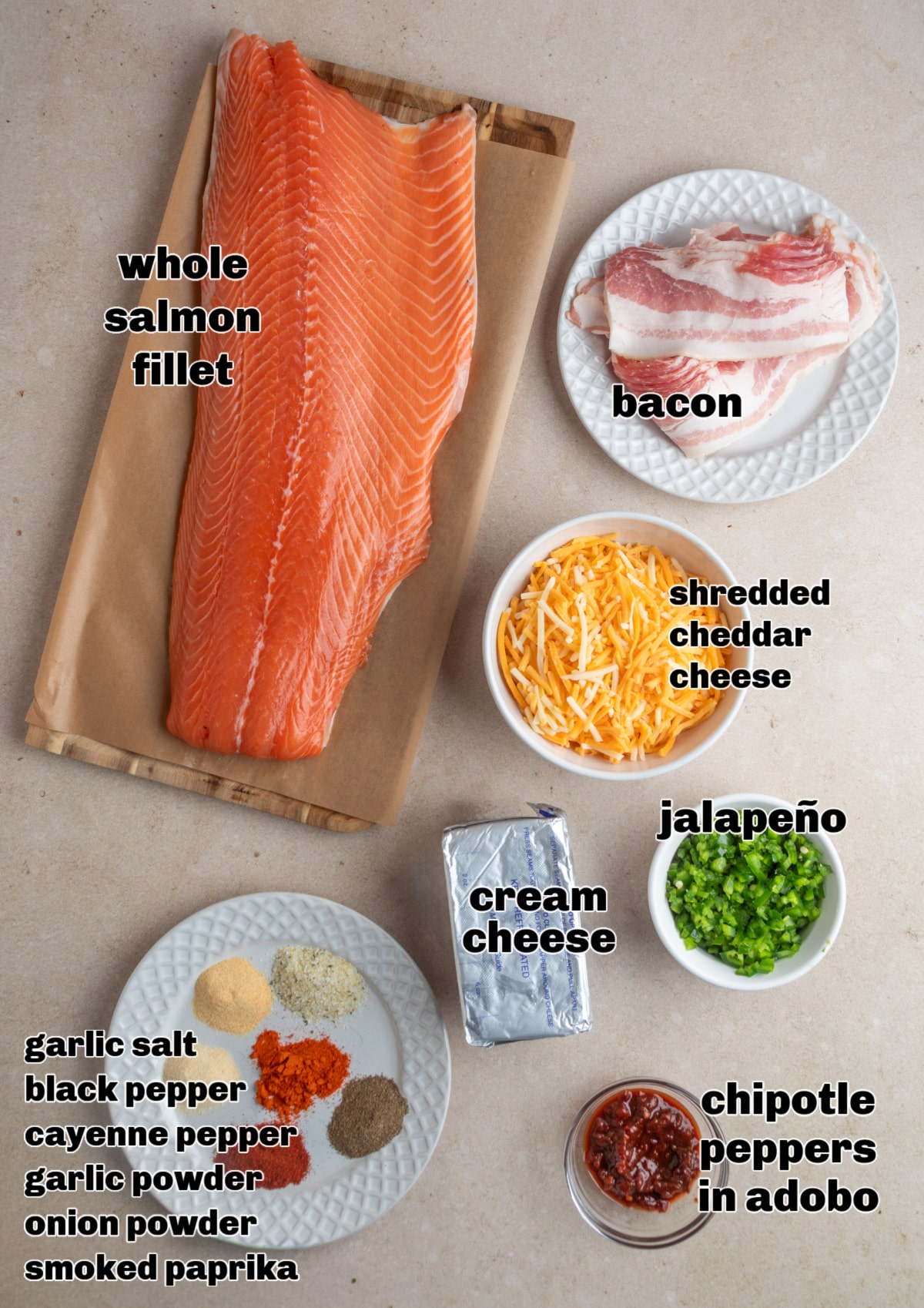 Whole salmon fillet, cream cheese, shredded cheddar, jalapeño, chipotle peppers in adobo, bacon, and spices laid out for making stuffed salmon rolls. Ingredients for chipotle jalapeño popper stuffed salmon rolls arranged on a work surface