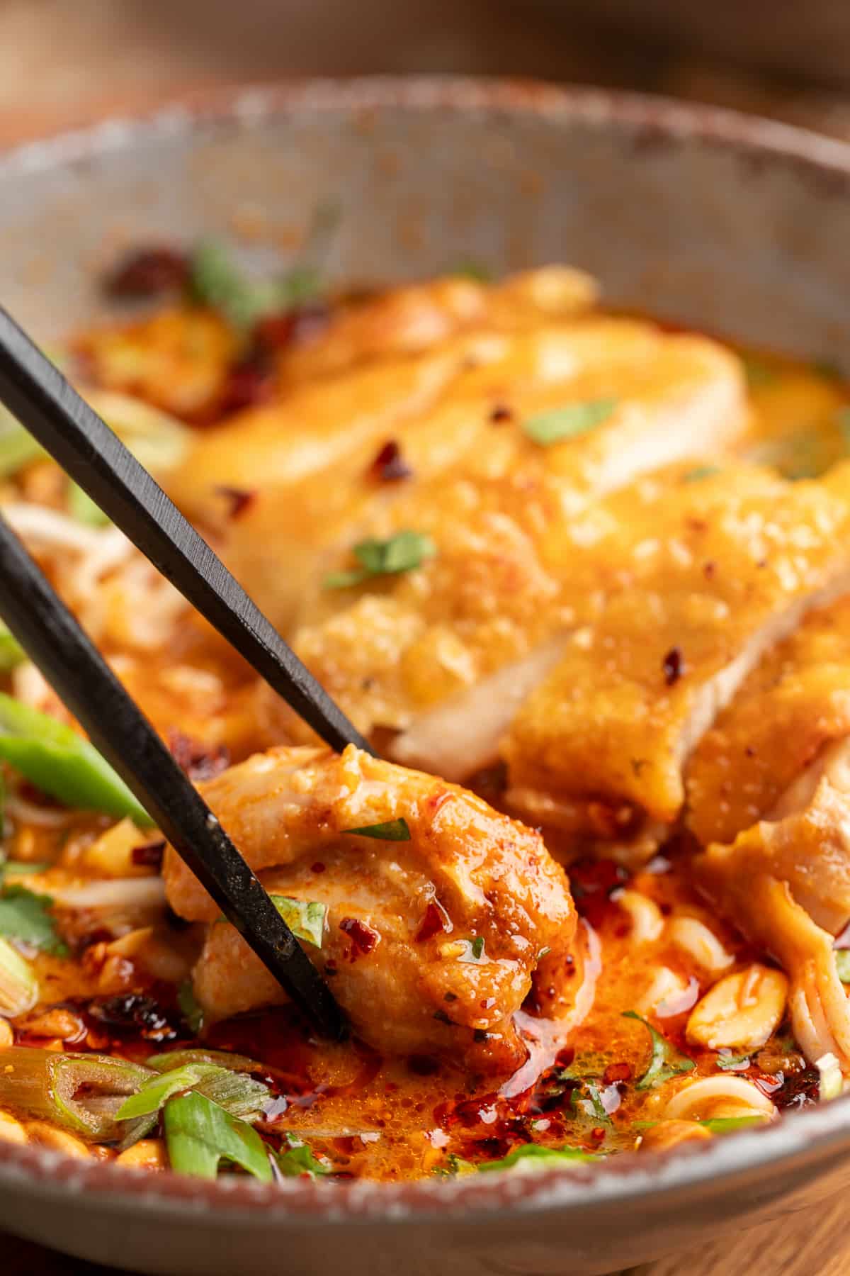 Crispy chicken ramen bite with coconut broth Chopsticks lifting a piece of crispy chicken from Thai coconut curry ramen with chili oil, scallions, and peanuts