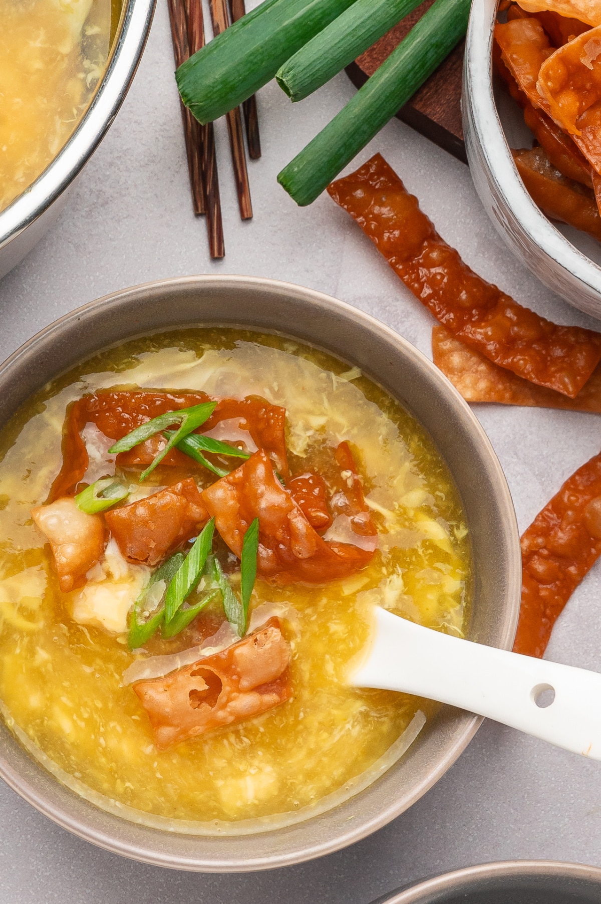 Overhead view of egg drop soup in a bowl with tender egg ribbons, topped with crispy fried wonton strips and sliced green onions Egg drop soup with crispy fried wonton strips and green onions