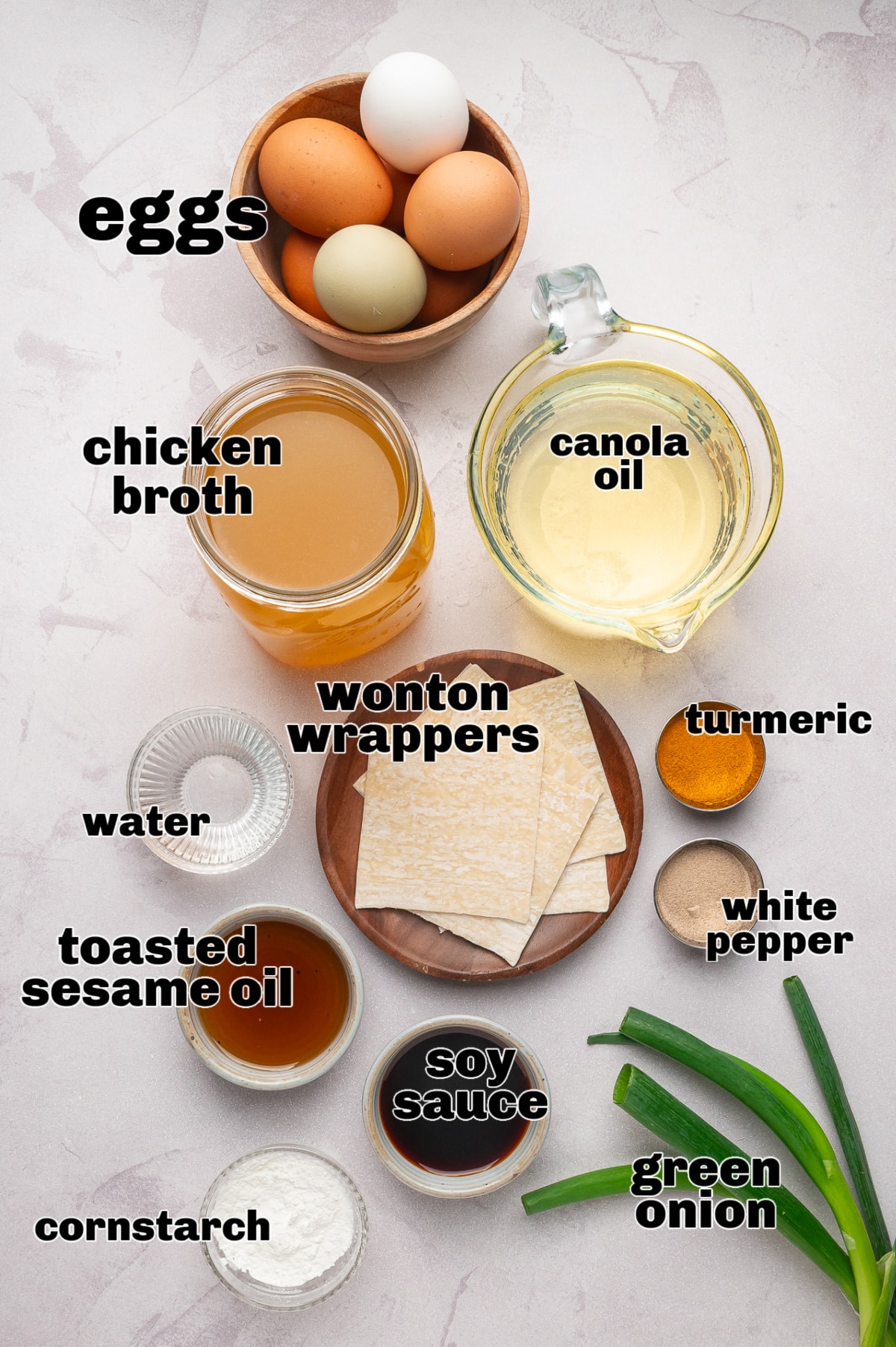 Ingredients for egg drop soup with fried wonton strips arranged on a light surface, including eggs, chicken broth, wonton wrappers, cornstarch, soy sauce, toasted sesame oil, white pepper, turmeric, and green onions Egg drop soup ingredients including eggs, chicken broth, wonton wrappers, and seasonings