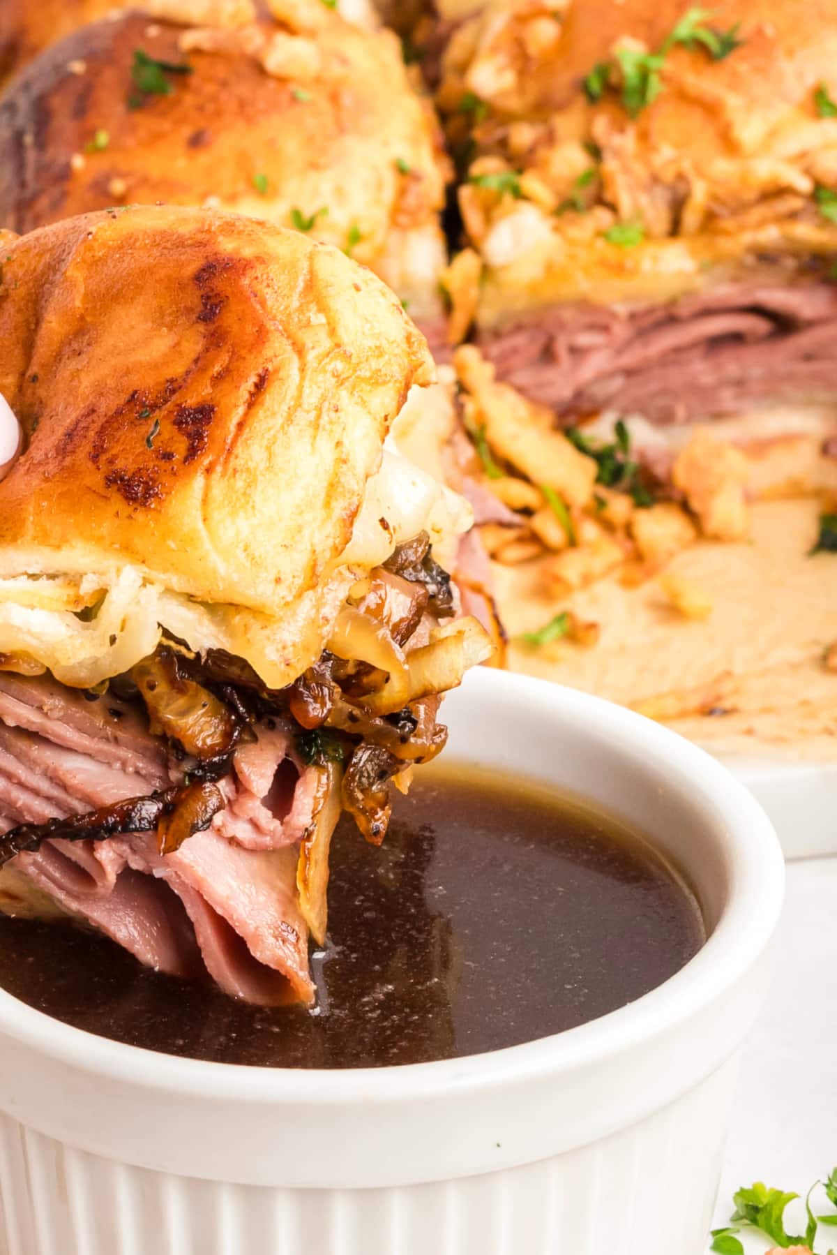 Close-up of a roast beef slider on a sweet roll being dipped into warm au jus, with caramelized onions and melted provolone cheese Roast beef slider dipped into au jus with caramelized onions and melted provolone