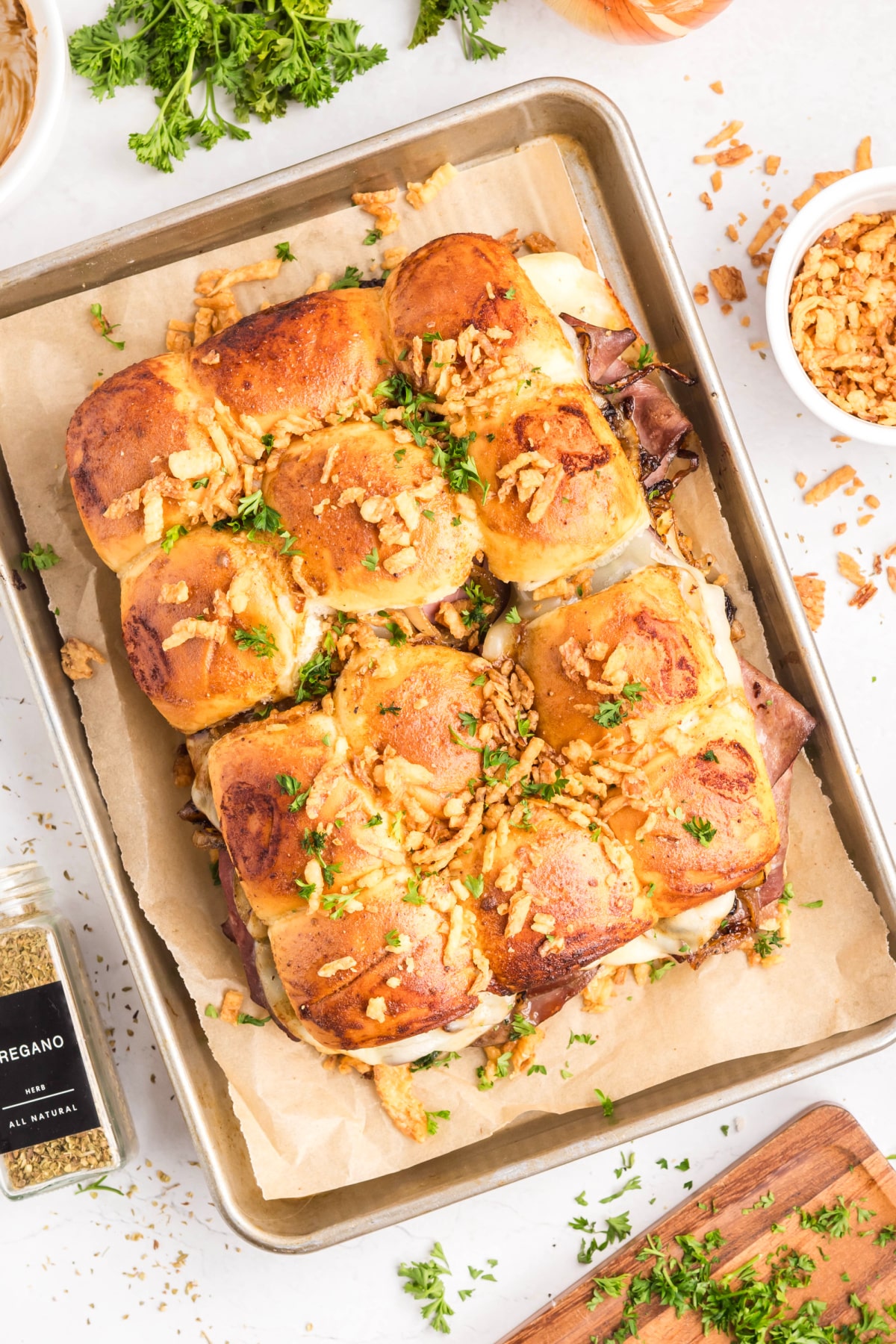 Overhead view of baked roast beef sliders on sweet rolls with melted provolone cheese, caramelized onions, French-fried onions, and chopped parsley Baked roast beef sliders with provolone, caramelized onions, and French-fried onions on sweet rolls