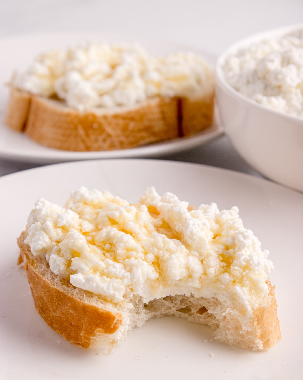 Close-up of fresh ricotta on toasted bread showing soft curds and creamy texture Fresh ricotta spread on bread with a bite taken out