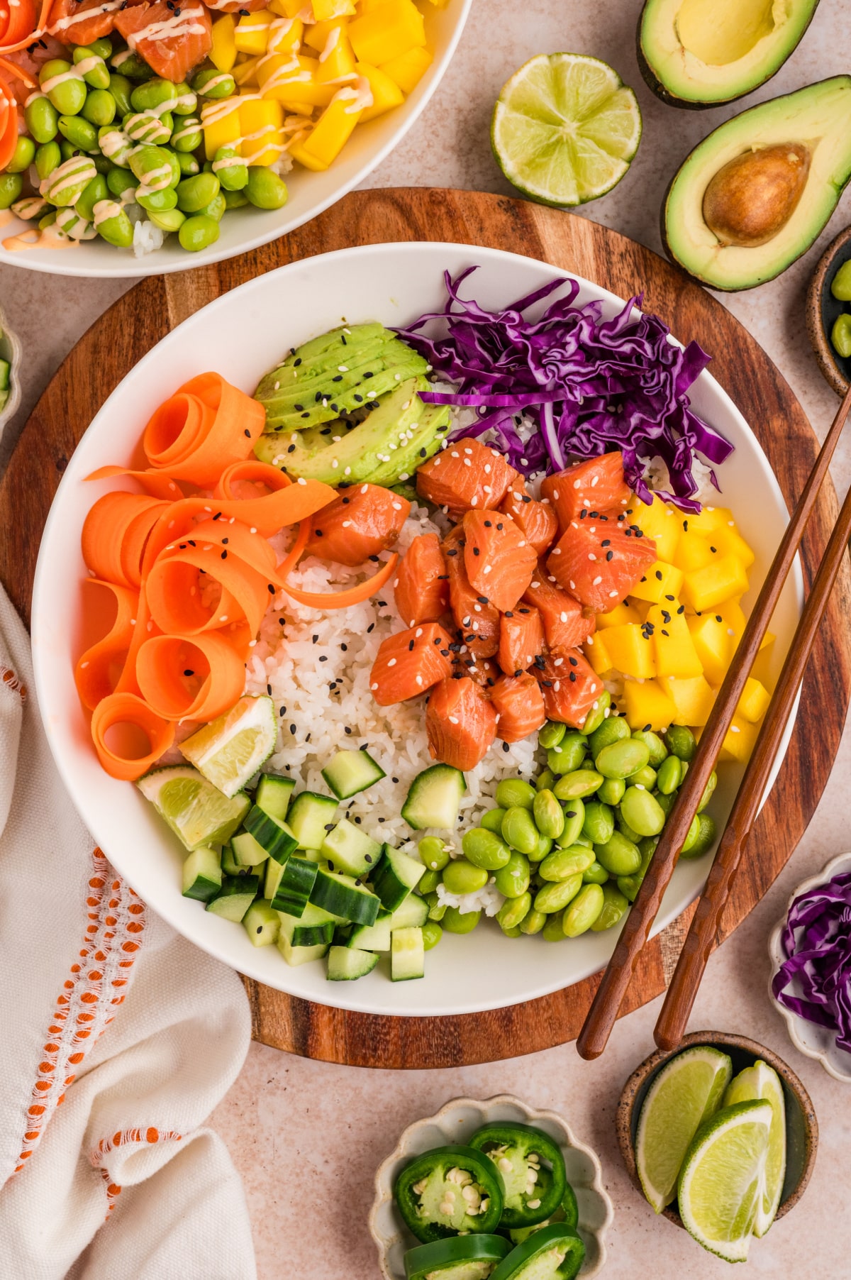 Overhead view of a salmon poke bowl with sushi rice, cubed salmon, mango, avocado, edamame, cucumber, shredded carrots, and purple cabbage Salmon poke bowls with marinated raw salmon, sushi rice, mango, avocado, and fresh vegetables
