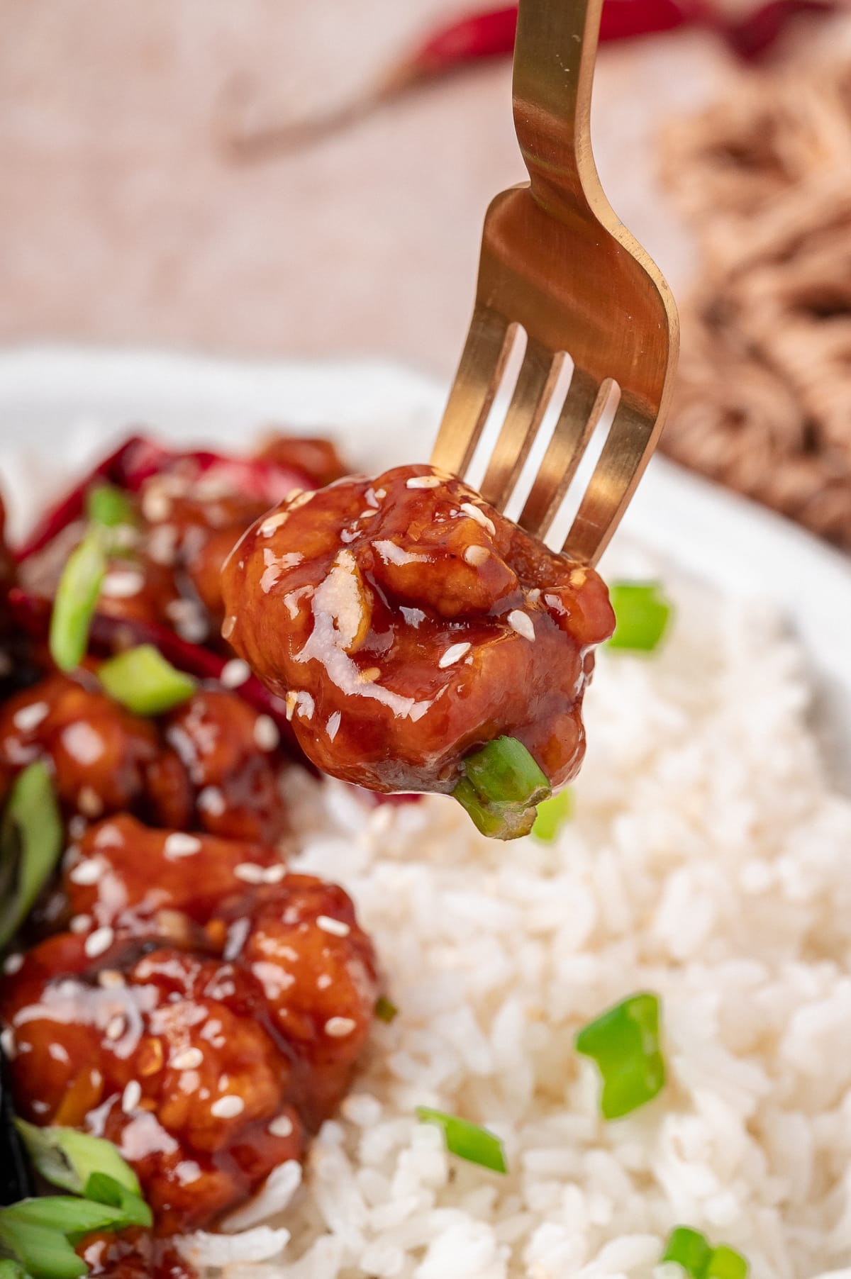 Close-up of glazed fried chicken piece on a fork over white rice with sesame seeds and scallions