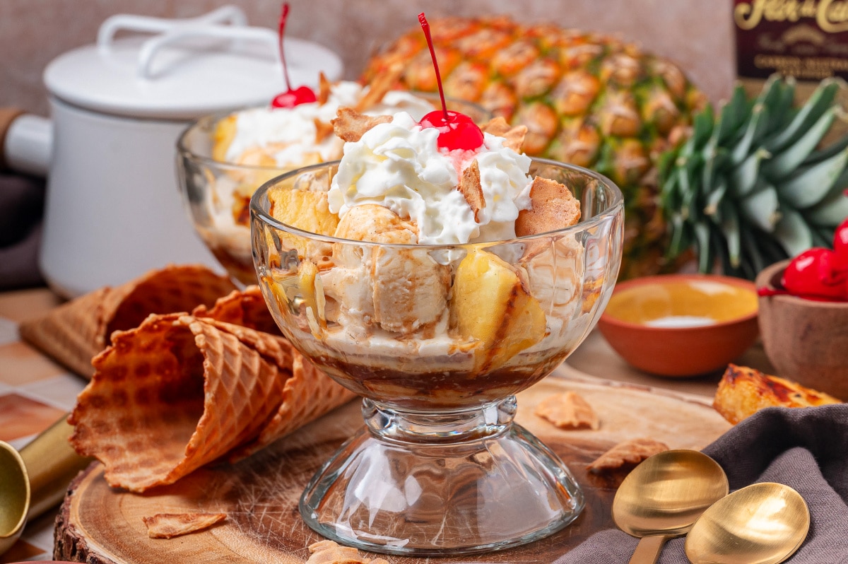 Grilled pineapple sundae with rum sauce, vanilla ice cream, and whipped cream served in a glass bowl