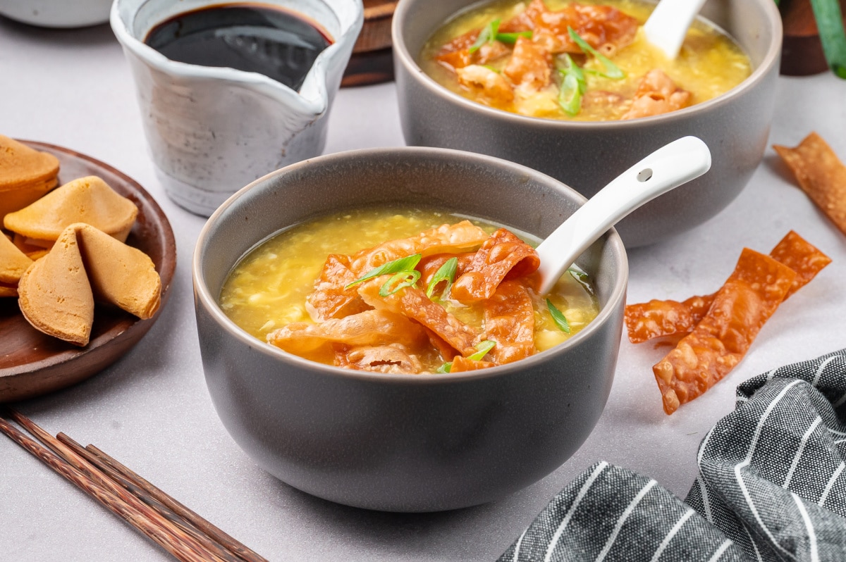 Two bowls of egg drop soup with tender egg ribbons, topped with fried wonton strips and sliced green onions, with chopsticks and sauce on the side Egg drop soup with fried wonton strips served in bowls