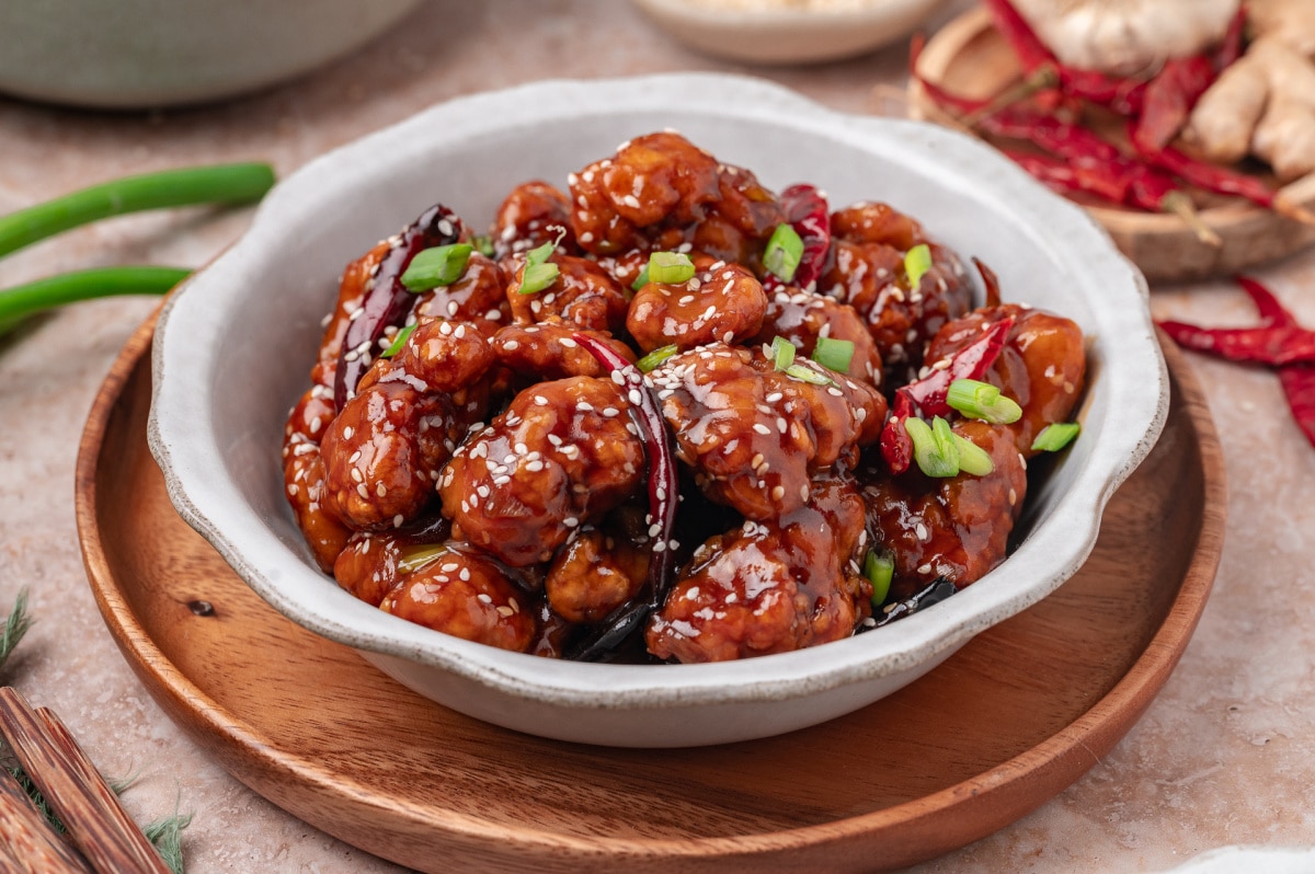 Close-up of General Tso’s chicken in a bowl with sesame seeds, scallions, and dried red chilies