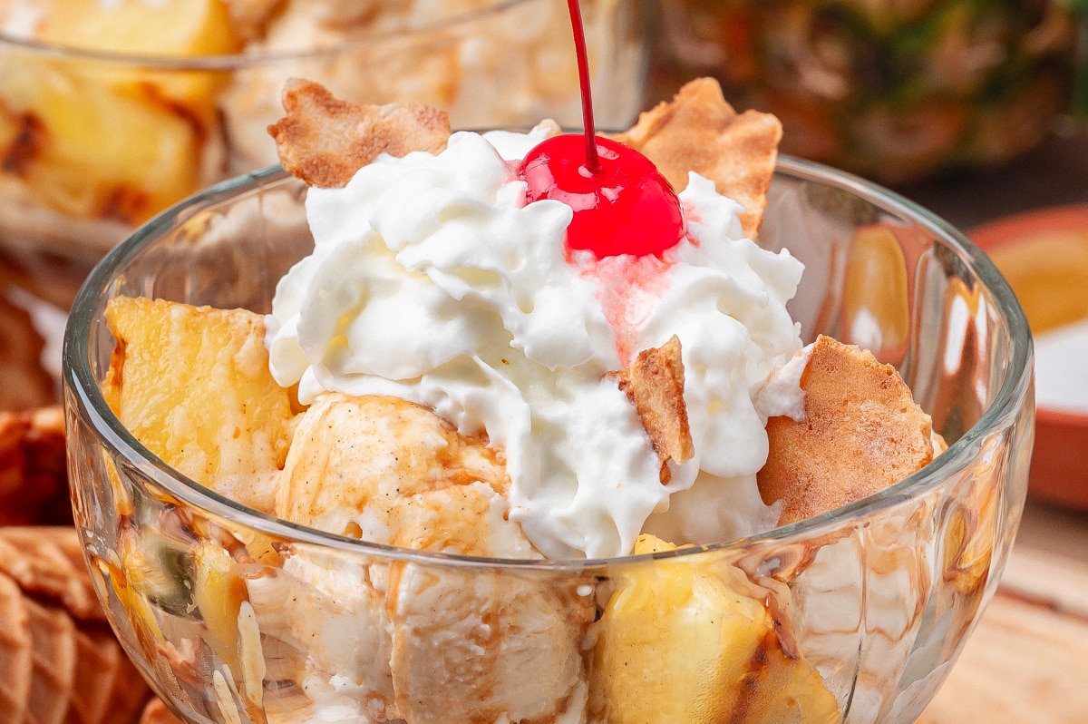 Close up of grilled pineapple with vanilla ice cream, whipped cream, and hot buttered rum sauce