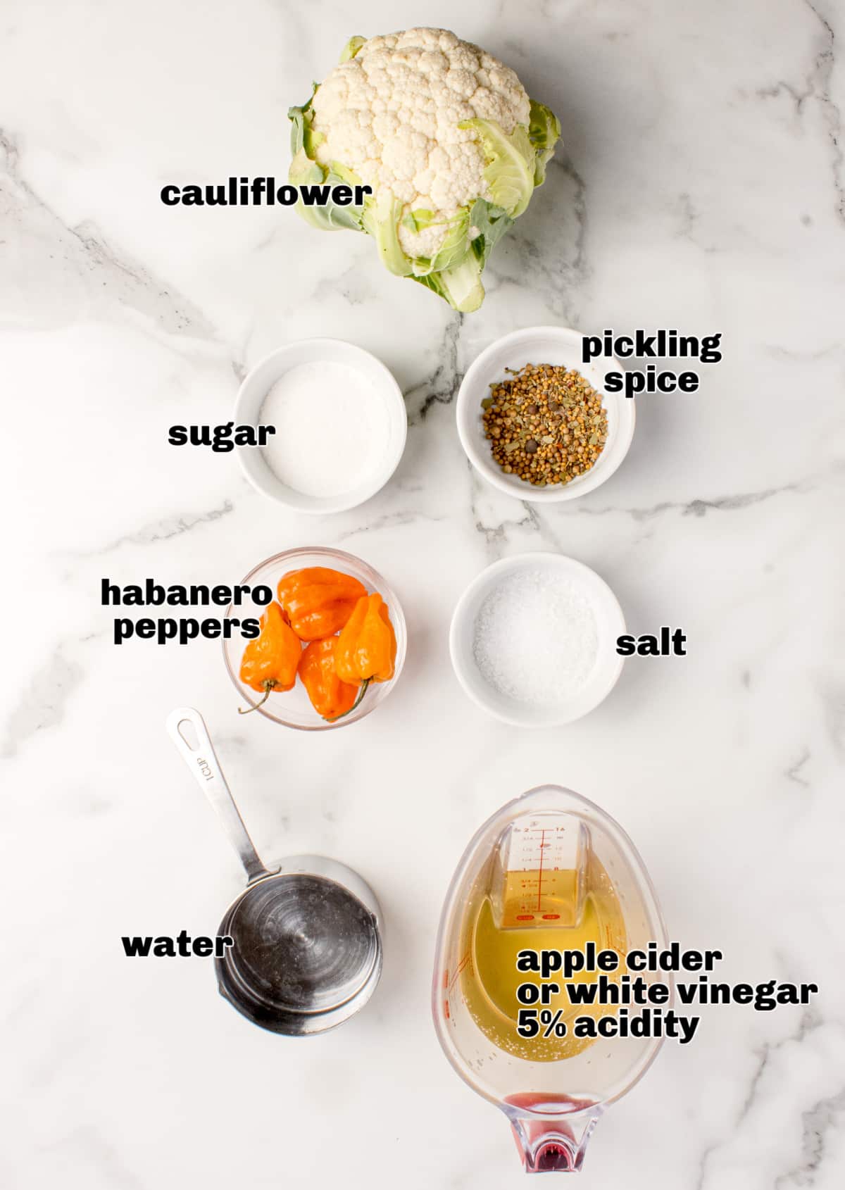 Hot pickled cauliflower ingredients laid out on marble surface Ingredients for hot pickled cauliflower including cauliflower, habaneros, pickling spice, vinegar, salt, sugar, and water