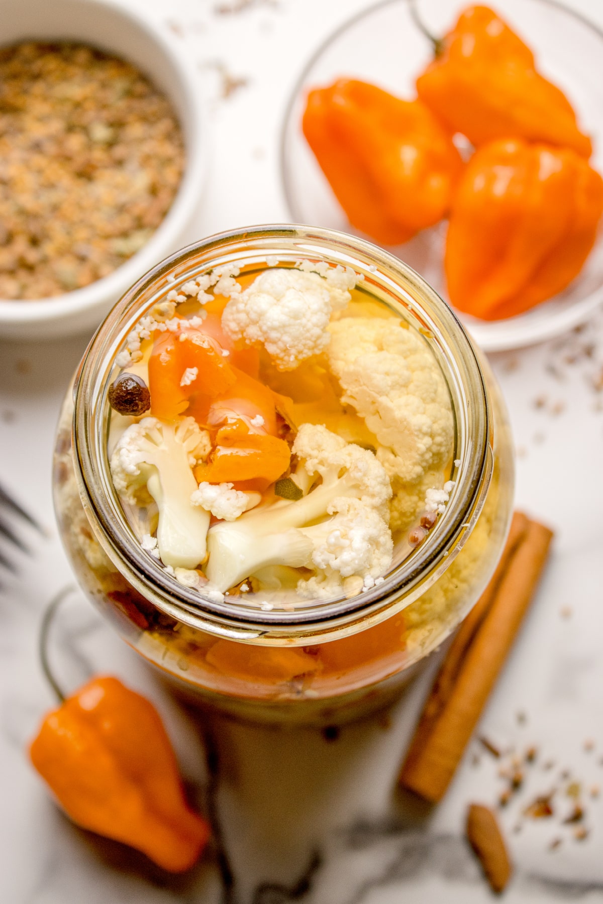 Jar of spicy cauliflower pickles with habanero peppers and pickling spice Hot pickled cauliflower in a glass jar with sliced habaneros and whole spices in vinegar brine