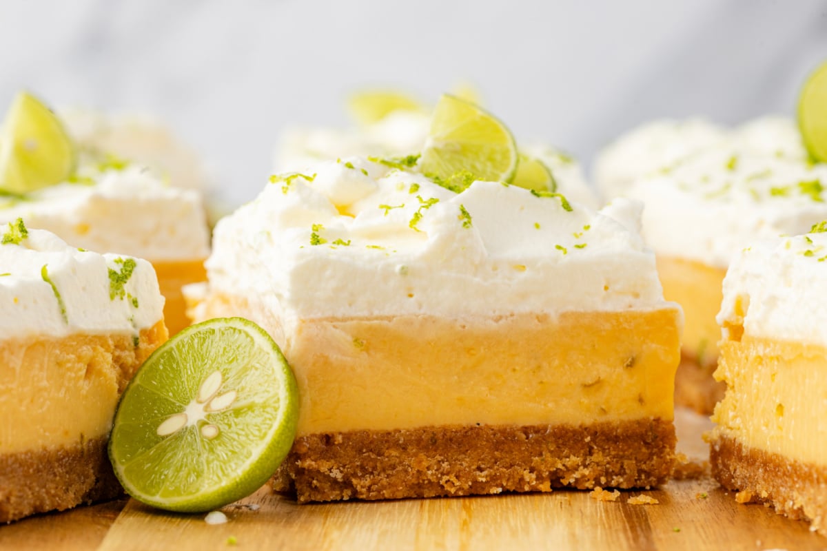 Clean layered slices with lime garnish Thick lime custard bars with whipped cream topping and graham cracker crust on wooden board