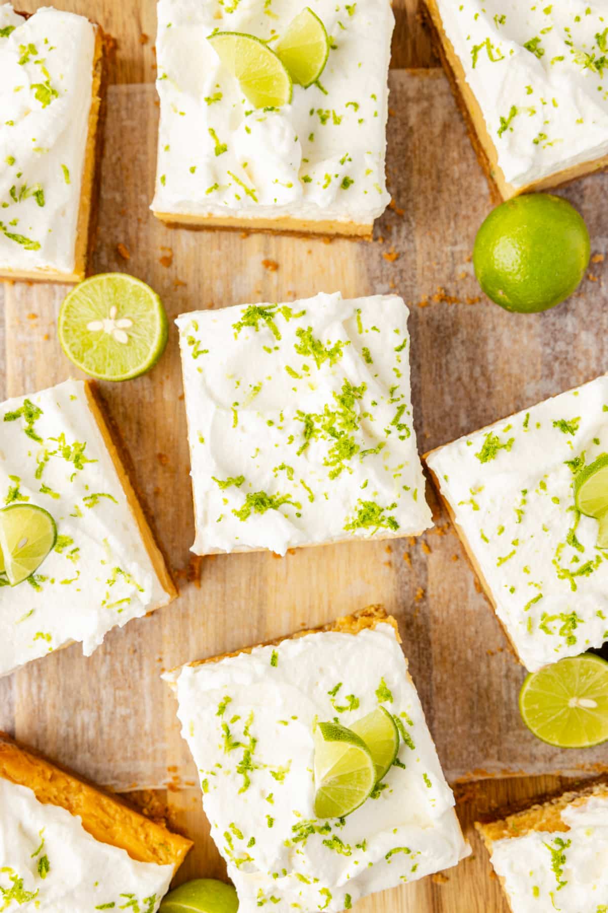 Overhead sliced squares with lime zest Overhead view of key lime bars topped with whipped cream and fresh lime zest on wooden board