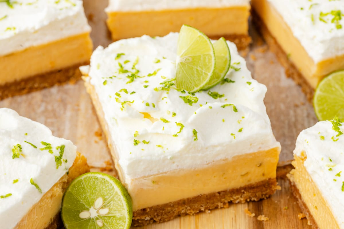 Square slice topped with lime wedges Key lime bars with thick custard filling, whipped cream topping, and fresh lime garnish