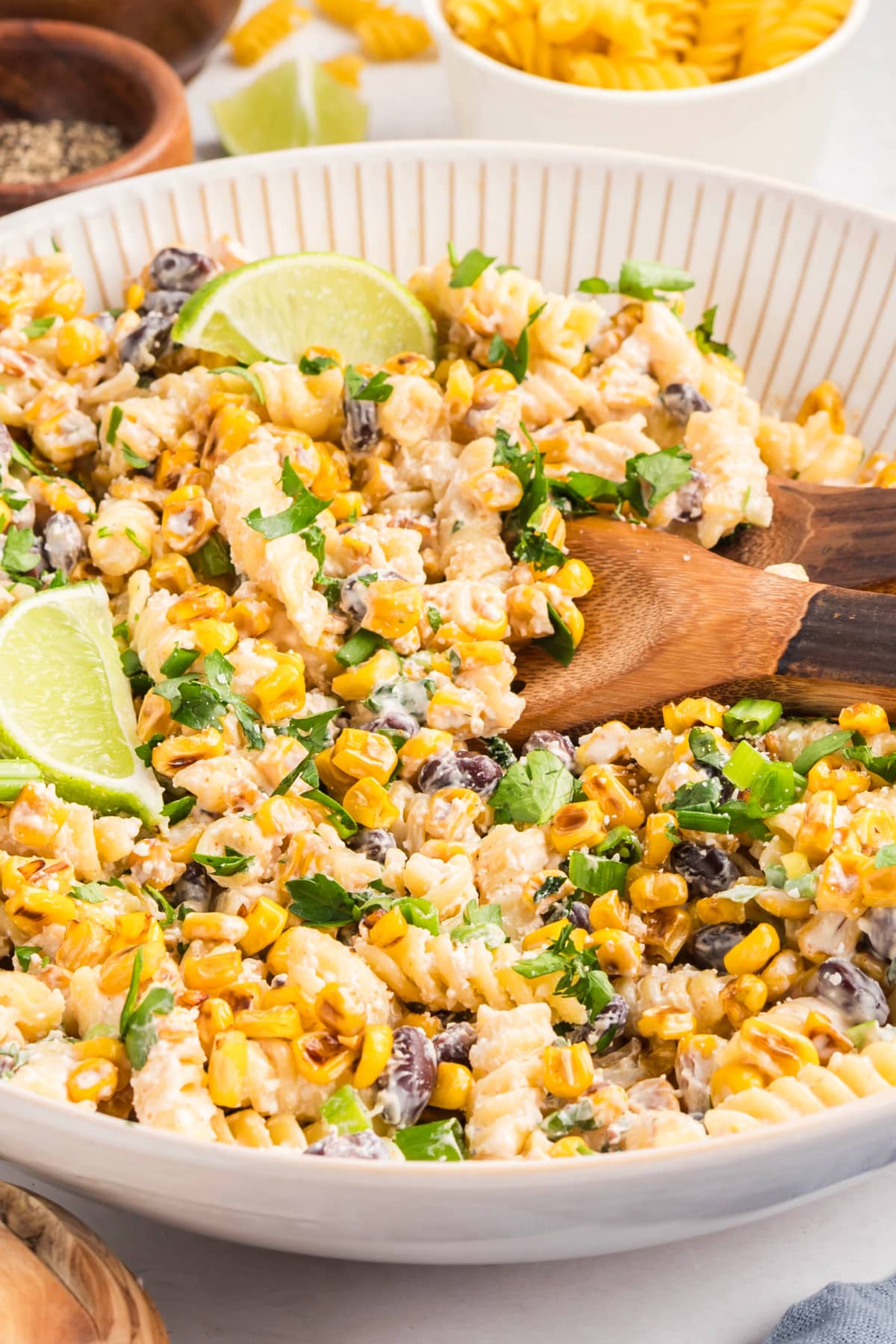 Creamy Mexican street corn pasta salad made with rotini pasta, sautéed corn, cotija, black beans, cilantro, and a chili-lime dressing, served in a white bowl with lime wedges Mexican street corn pasta salad with golden sautéed corn, cotija cheese, cilantro, and lime wedges in a serving bowl