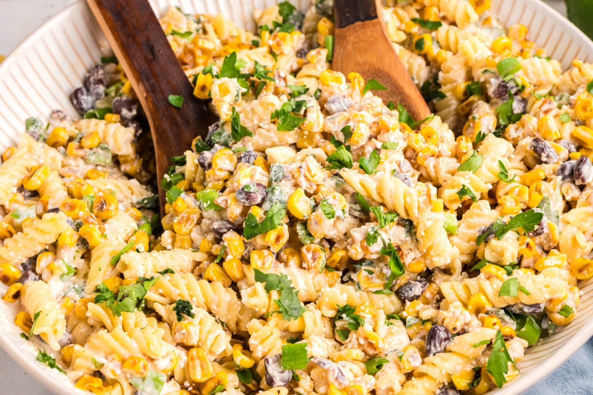 Mexican street corn pasta salad in a shallow serving bowl with sautéed corn, rotini pasta, black beans, cotija cheese, cilantro, and lime wedges Creamy street corn pasta salad with rotini, golden corn, black beans, cotija, and fresh cilantro in a large serving bowl