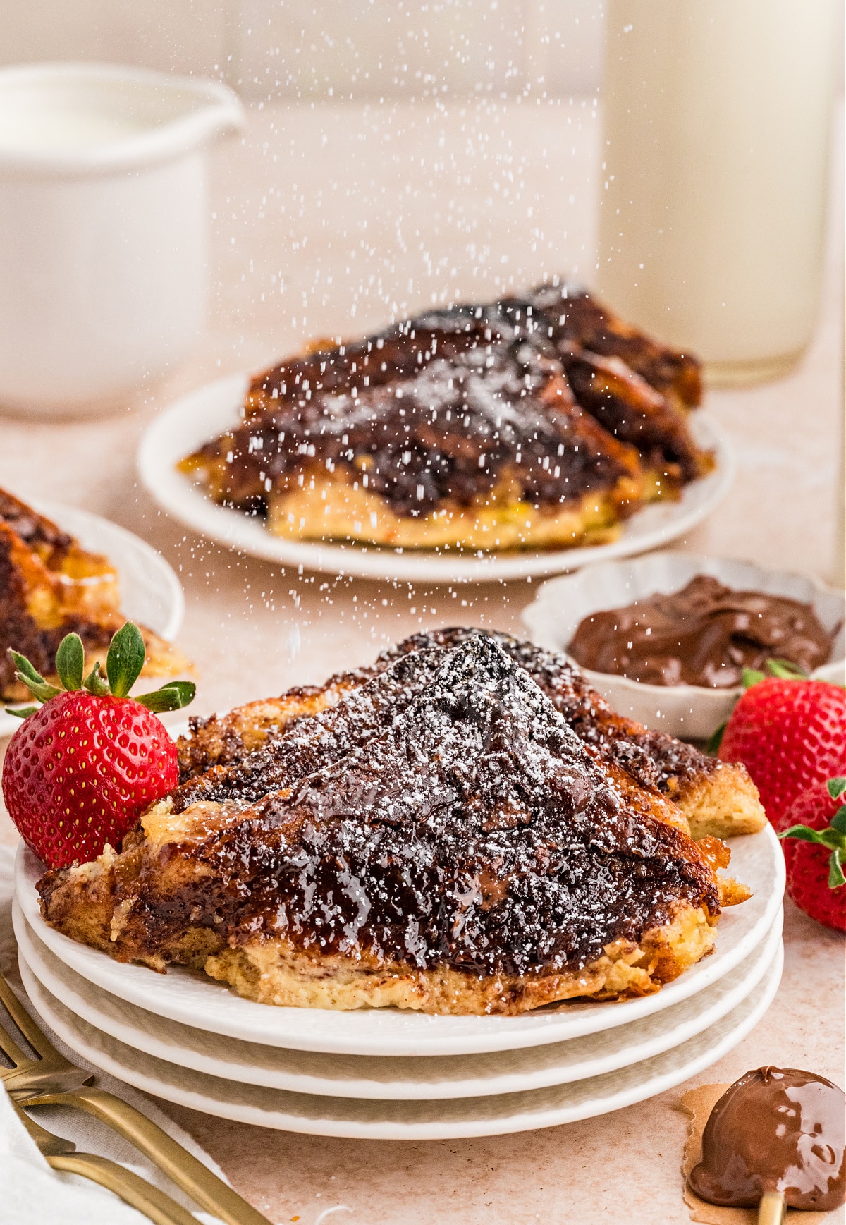 Nutella French Toast Bake slice dusted with powdered sugar, served with fresh strawberries on a white plate