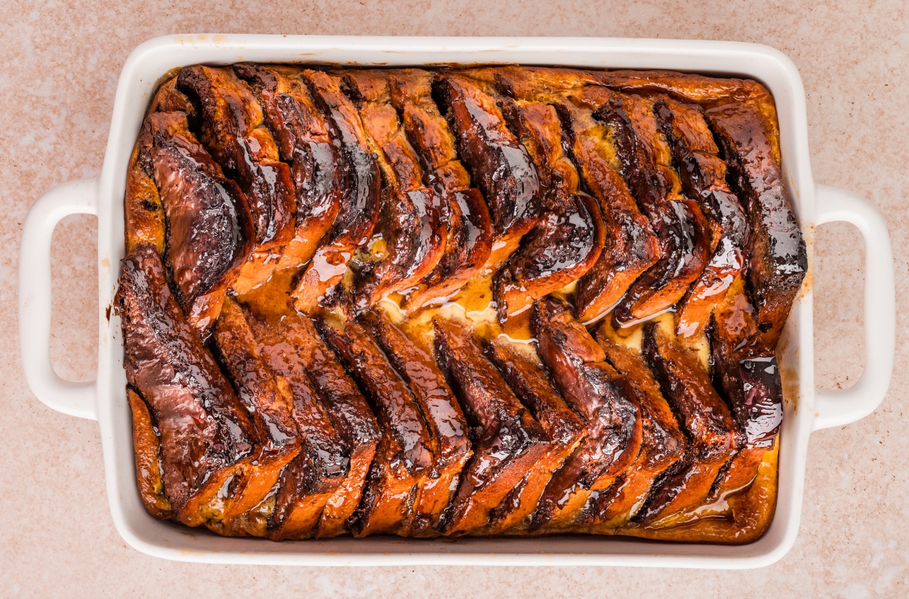 Overhead view of baked chocolate hazelnut French toast casserole in a white 9x13 dish with glossy brown sugar topping