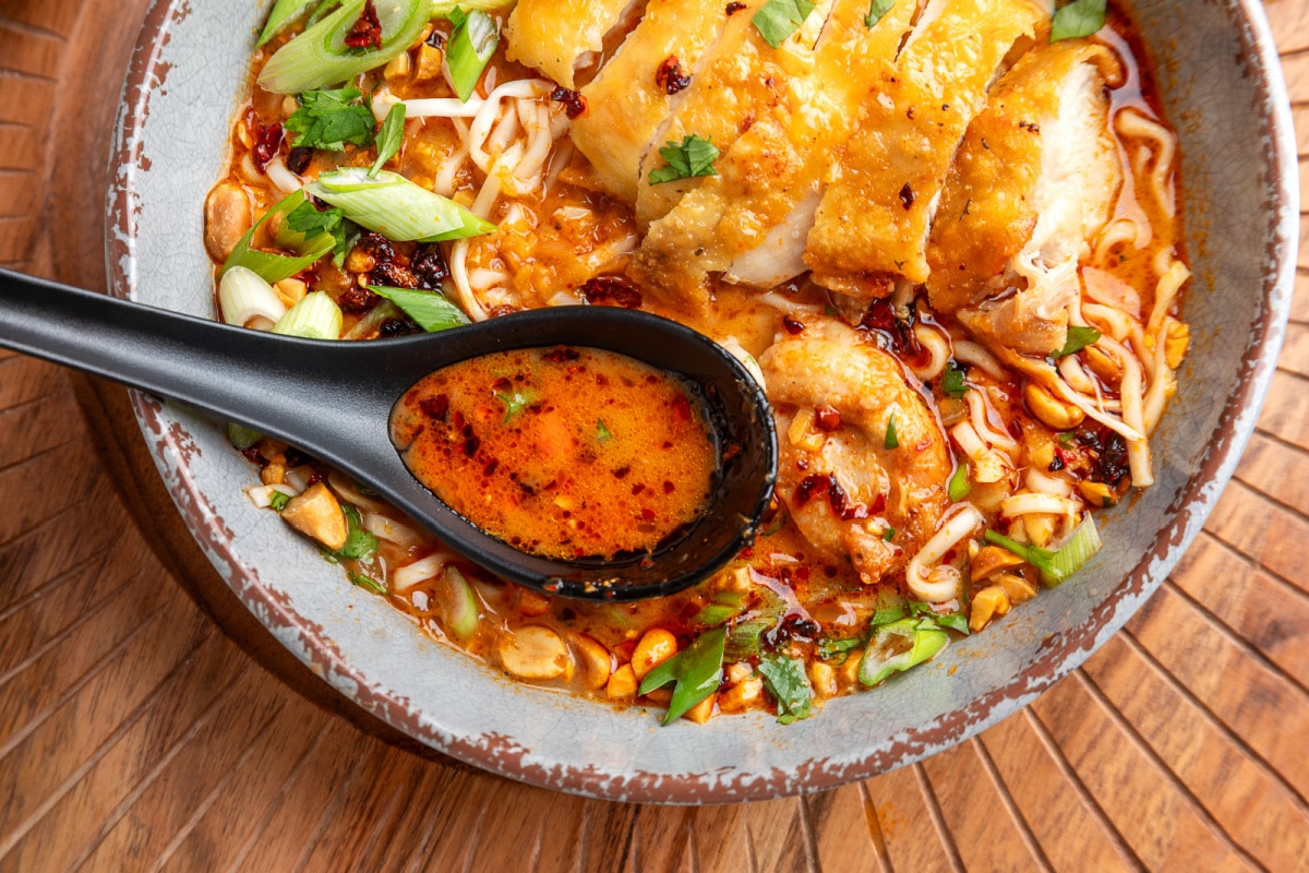 Panang curry ramen broth close up Spoonful of coconut broth from panang curry ramen with crispy chicken, chili oil, scallions, and peanuts