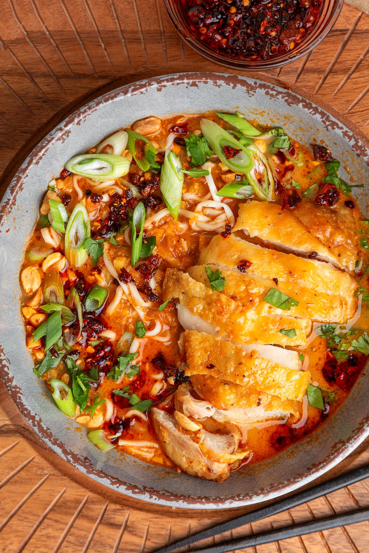 Crispy chicken panang ramen bowl Panang curry ramen topped with sliced crispy chicken thighs, chili crunch, scallions, cilantro, and peanuts