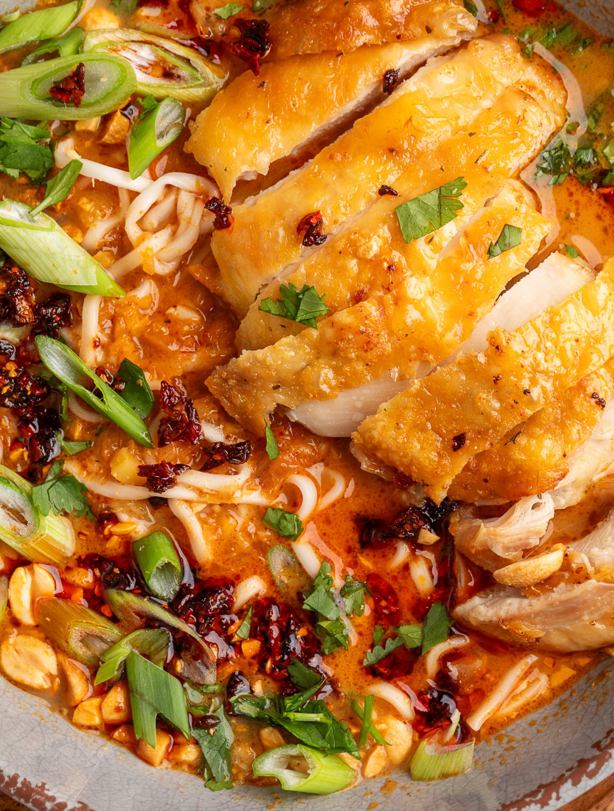 Panang curry ramen with crispy chicken detail Panang curry ramen with crispy chicken sliced over coconut curry broth, ramen noodles, chili crunch, scallions, cilantro, and peanuts