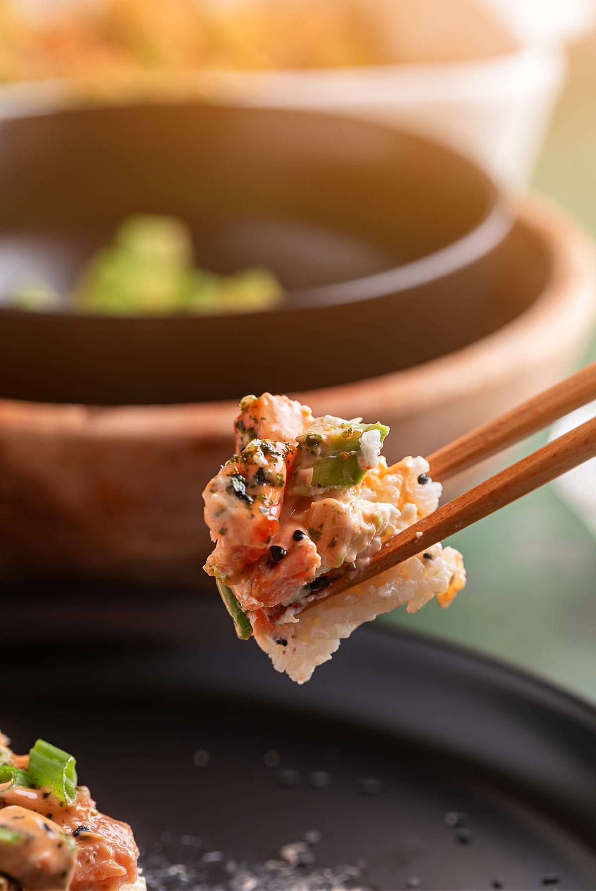 Salmon Crab Sushi Bake lifted with chopsticks for serving. Salmon Crab Sushi Bake bite held with chopsticks showing rice, crab, salmon, and spicy mayo