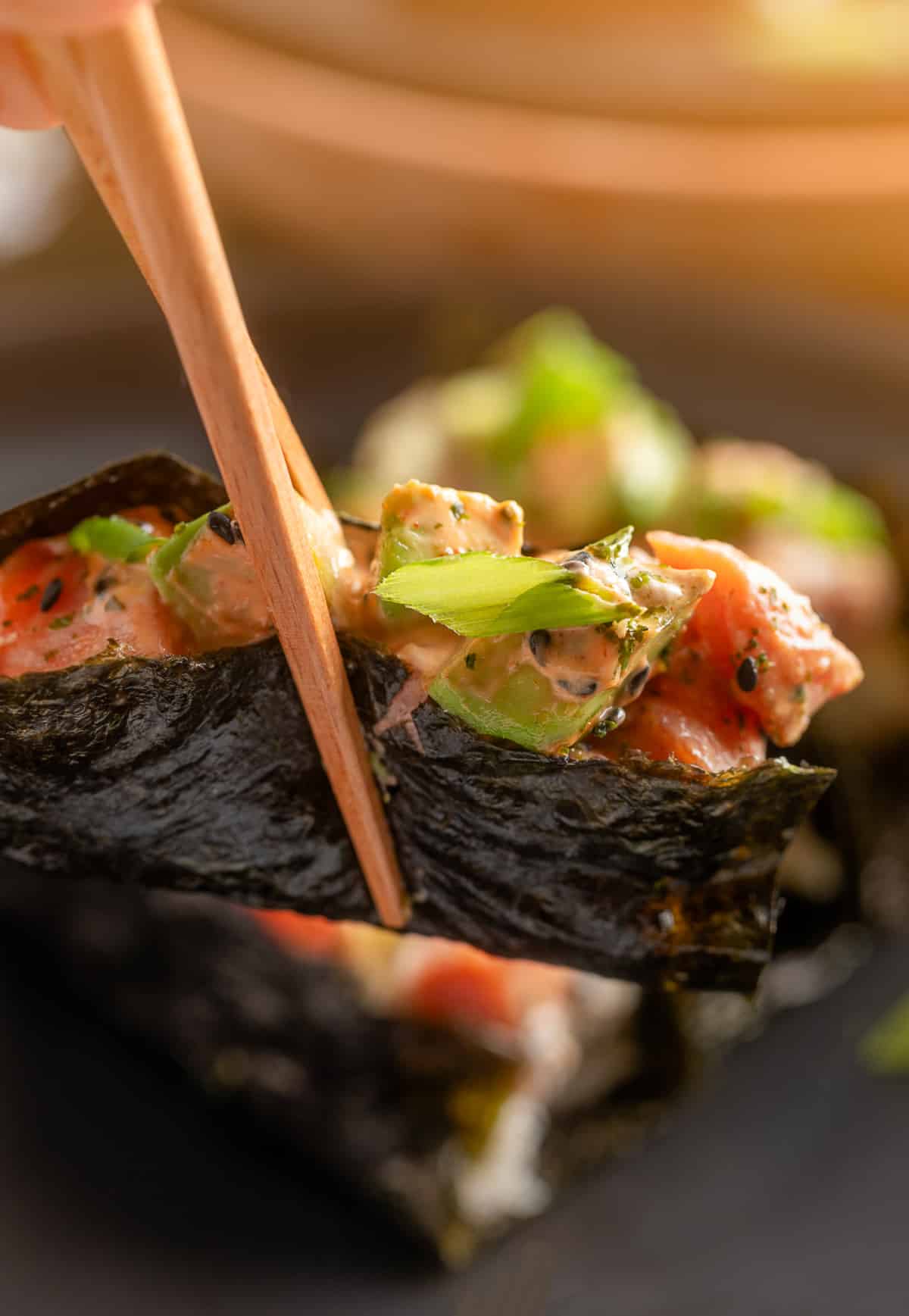 Close-up of sushi bake scooped into nori with toppings. Nori-wrapped sushi bake topped with salmon, avocado, and spicy mayo