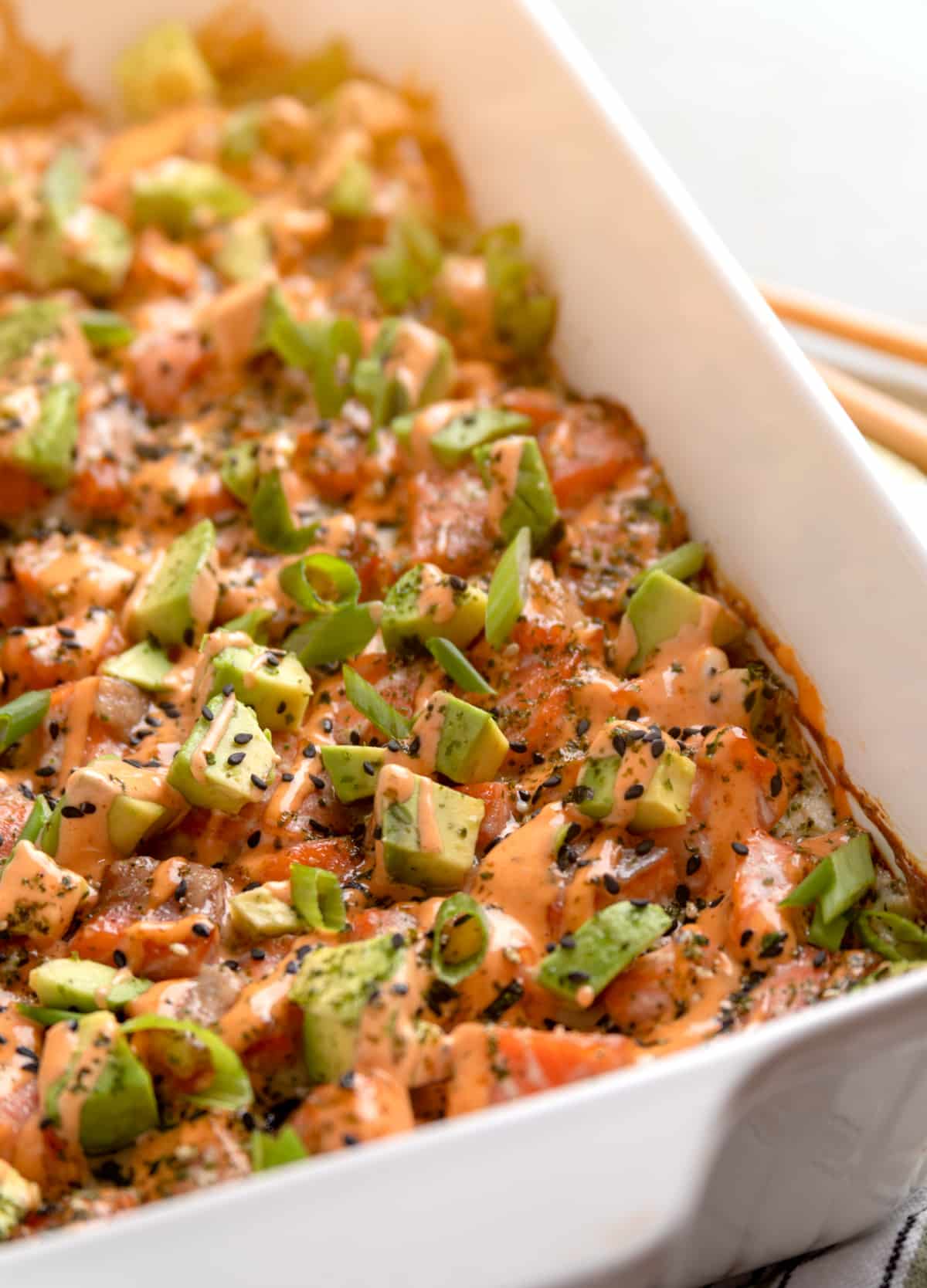 Salmon Crab Sushi Bake fresh from the oven in a 9x13 baking dish. Salmon Crab Sushi Bake baked in a 9x13 dish topped with spicy mayo, avocado, and green onions